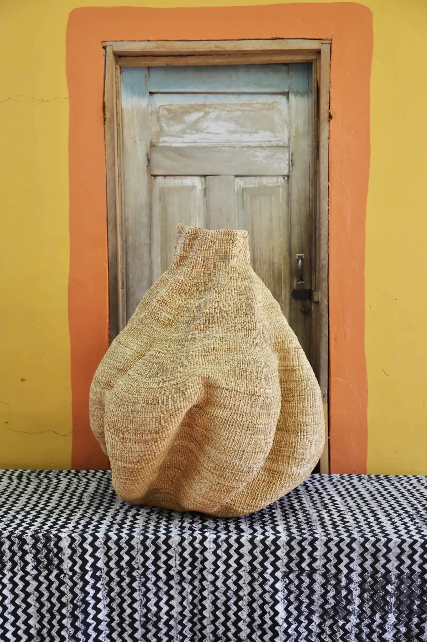 A handwoven piece with decorative curves sitting on a black and white cloth against a wooden door