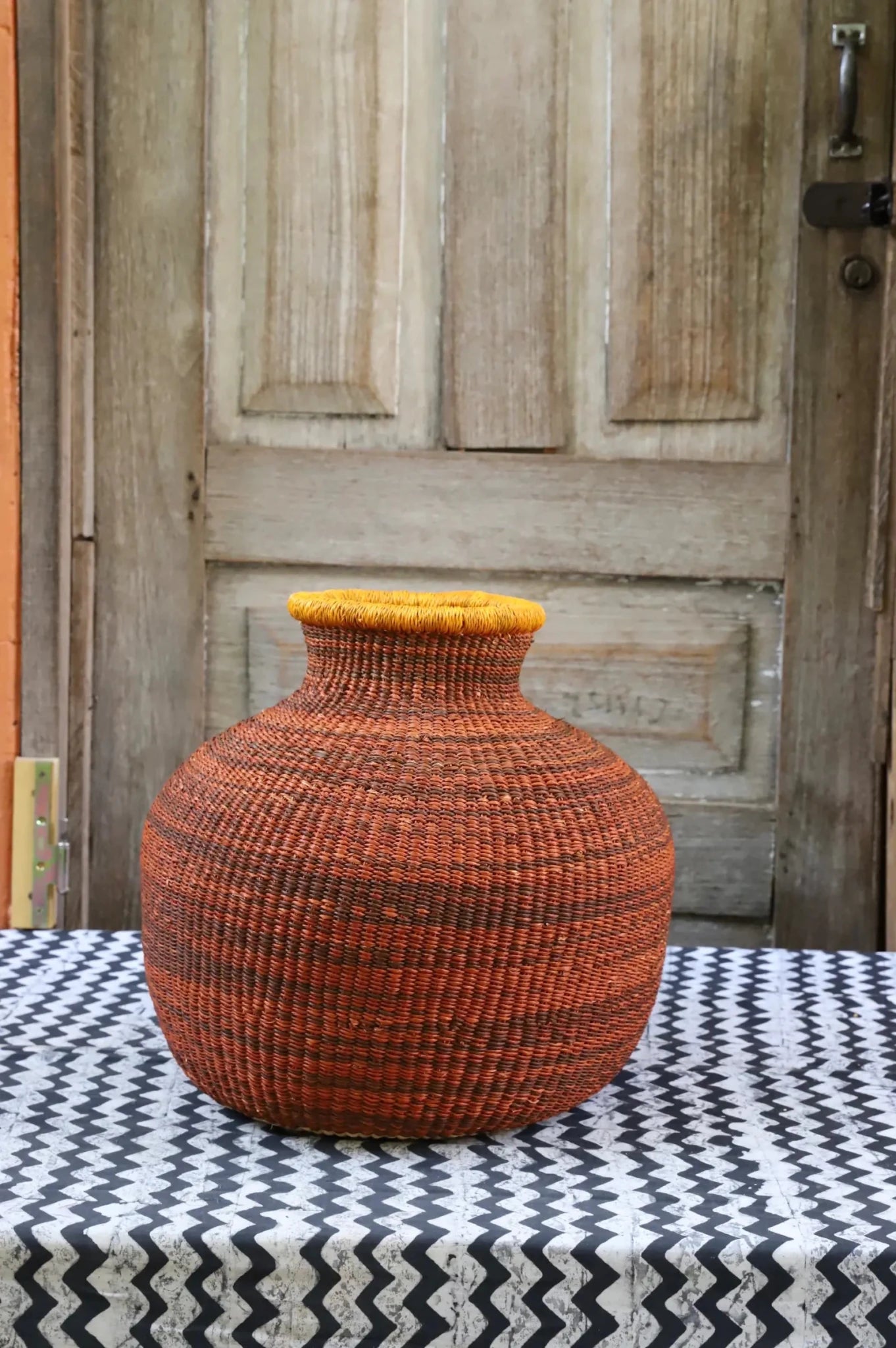 Decorative handwoven basket with colorful patterns on a black and white cloth against a wooden door.