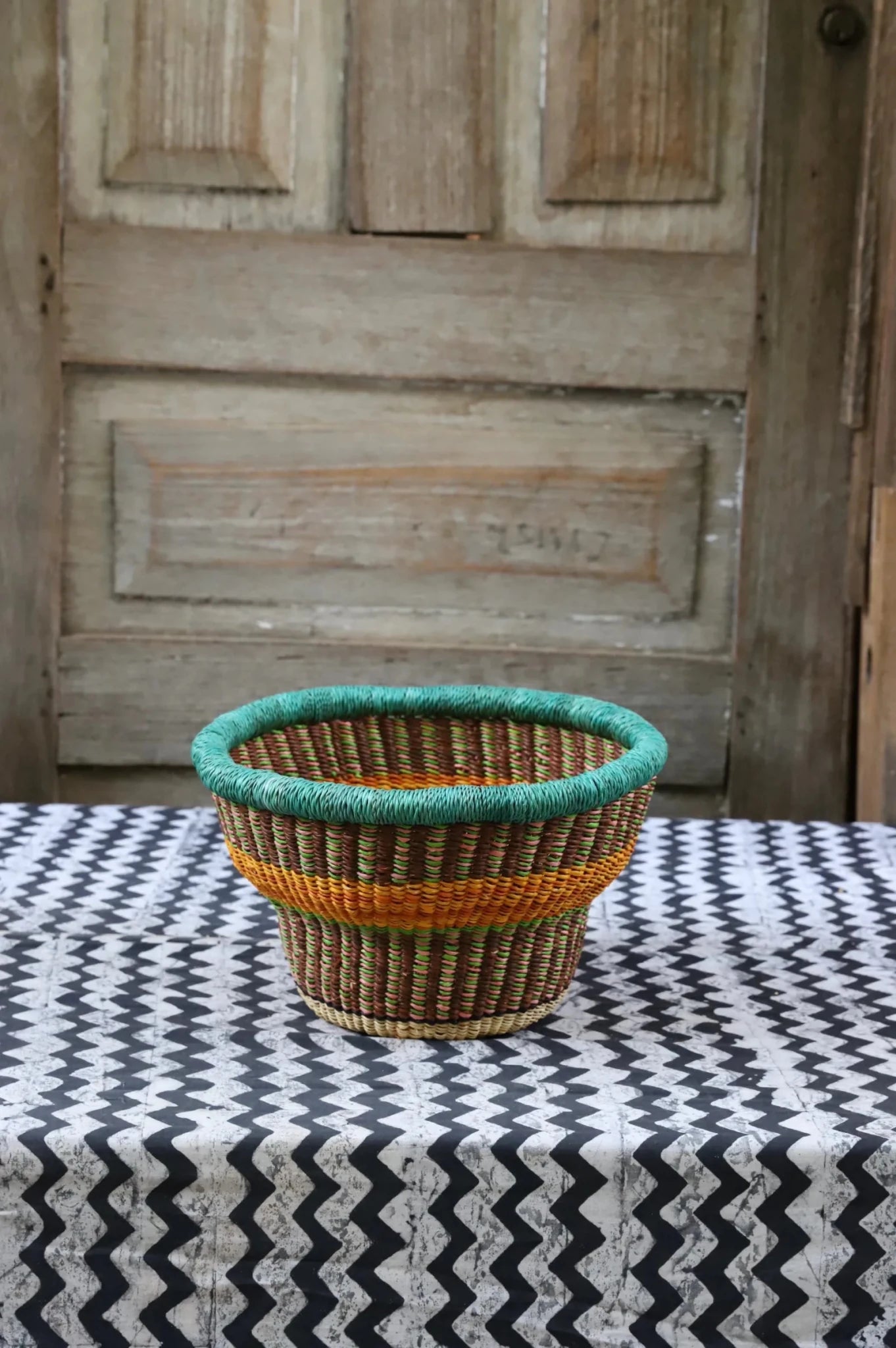 Woven storage basket with a beautiful pattern on a black and white cloth against a wooden door.