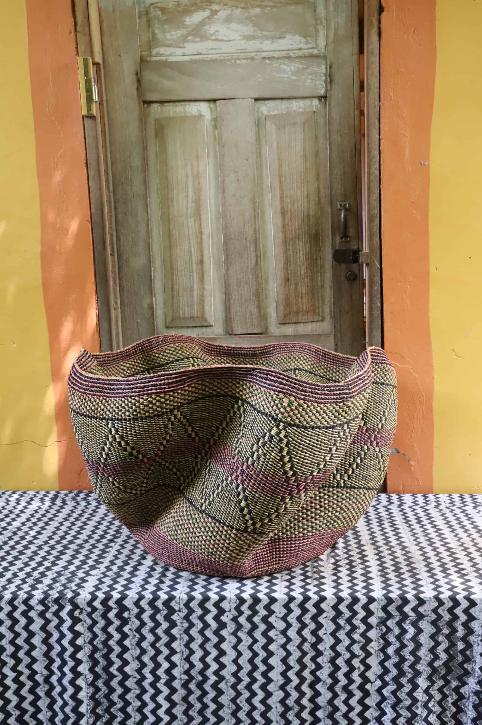 Giant Wave art basket with an olive green and dark brown diamond pattern on a black and white cloth before a wooden door.