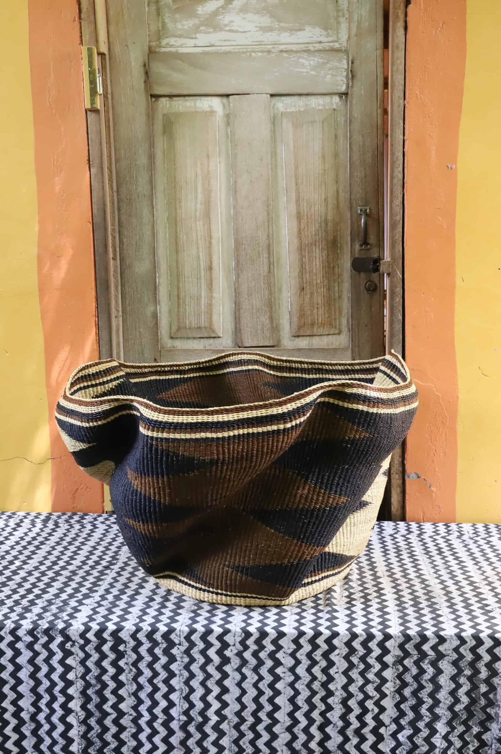 Giant Wave art basket with bold black wave bands, side view, on a black and white cloth before a wooden door.