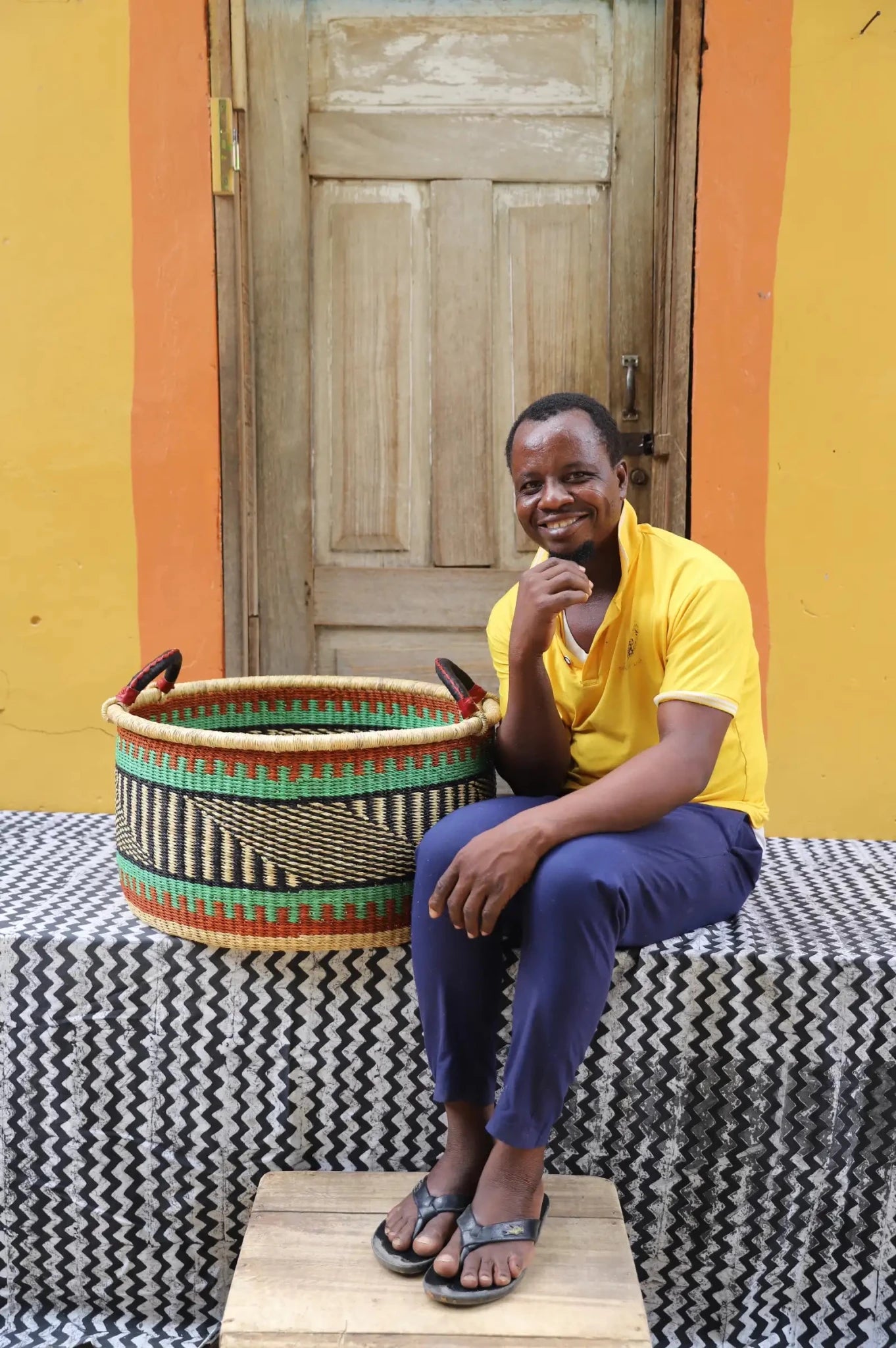 Woven Tub (Large) with man weaver handwoven in Ghana sitting on black and white cloth and wooden door in background