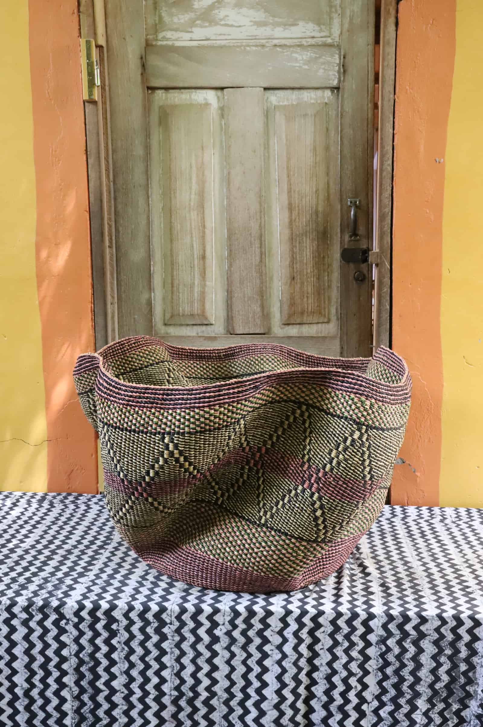 Giant Wave art basket with an olive green and dark pattern, angled view, on a black and white cloth before a wooden door.