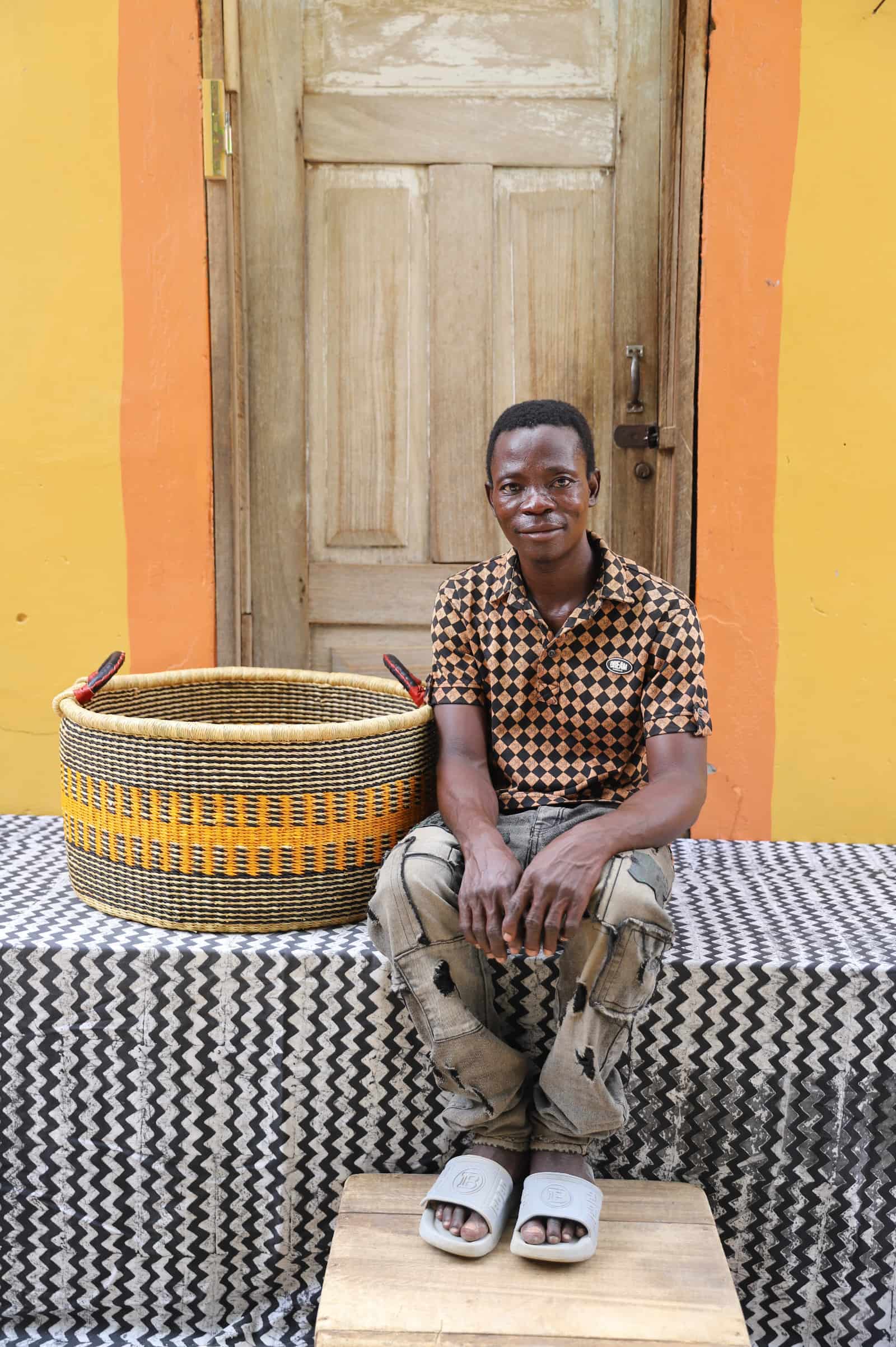 Woven Tub (Large) with woman weaver handwoven in Ghana sitting on black and white cloth and wooden door in background


