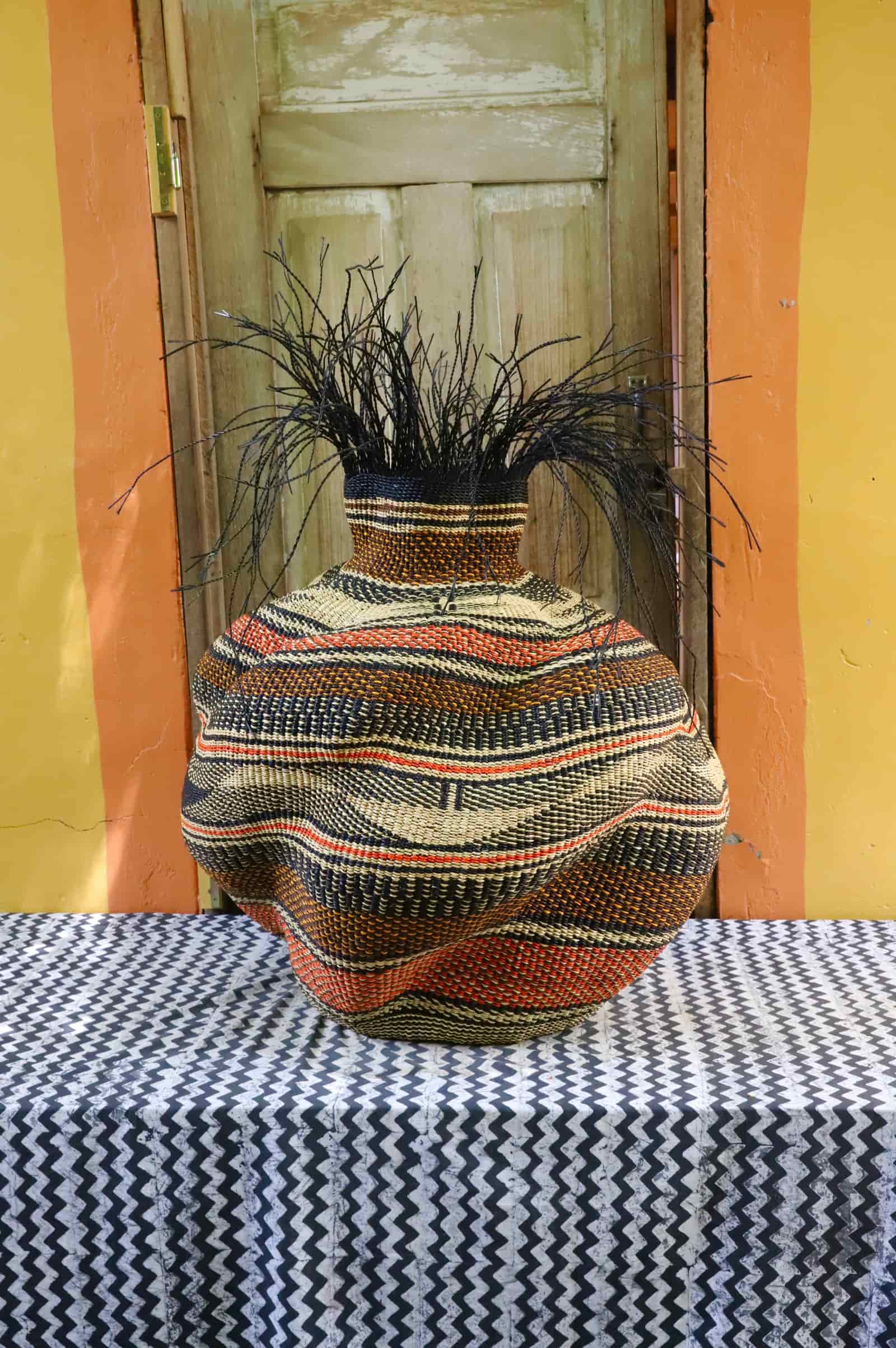Large Tua-Tia baobab art basket in dark terracotta and natural wave pattern with black straw, on chevron cloth.
