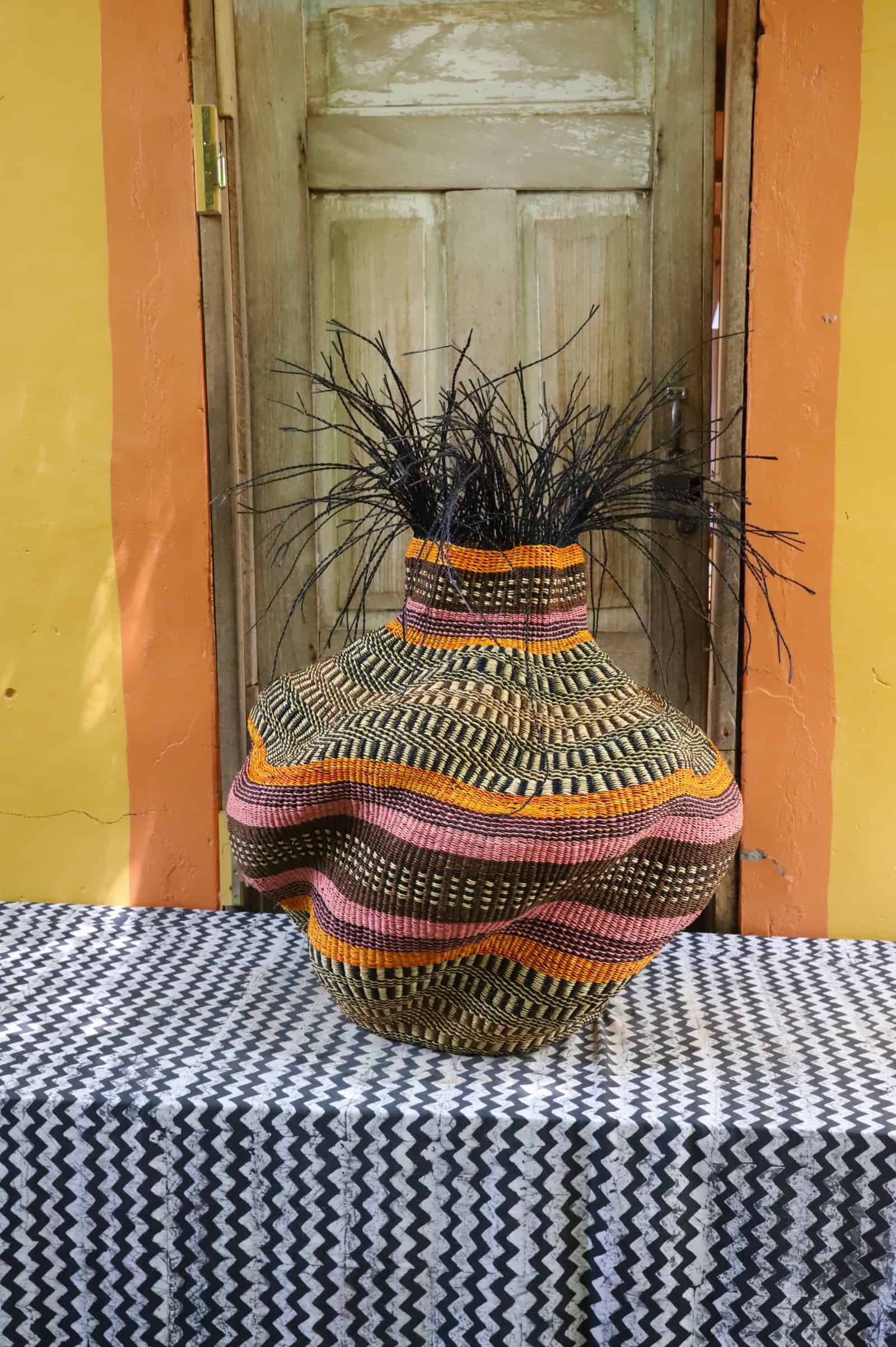 Medium Tua-Tia baobab art basket in dark, orange and pink stripes with black straw branching, on chevron cloth.