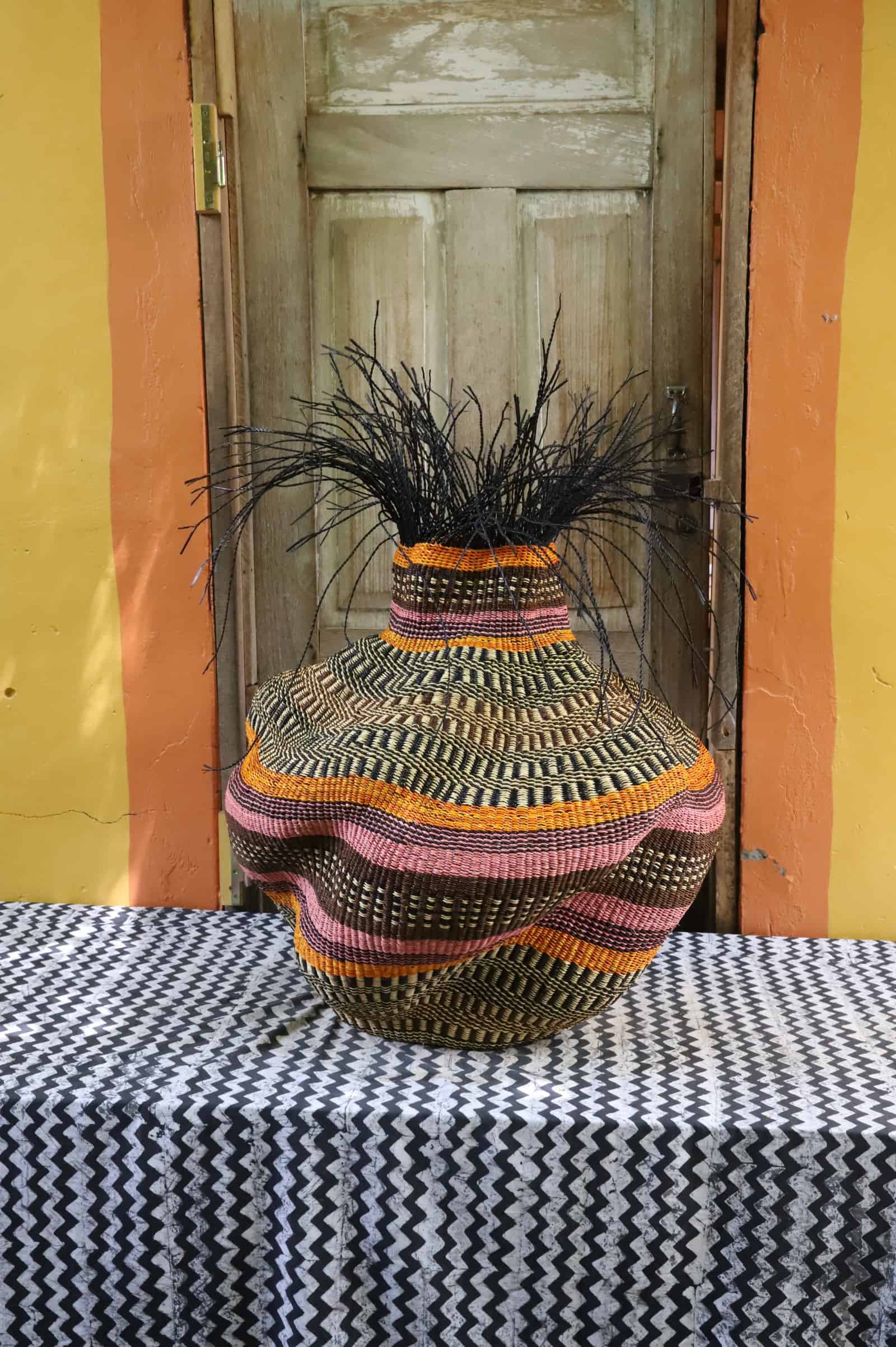 Medium Tua-Tia baobab art basket in dark, orange and pink stripes with black straw, front view on chevron cloth.