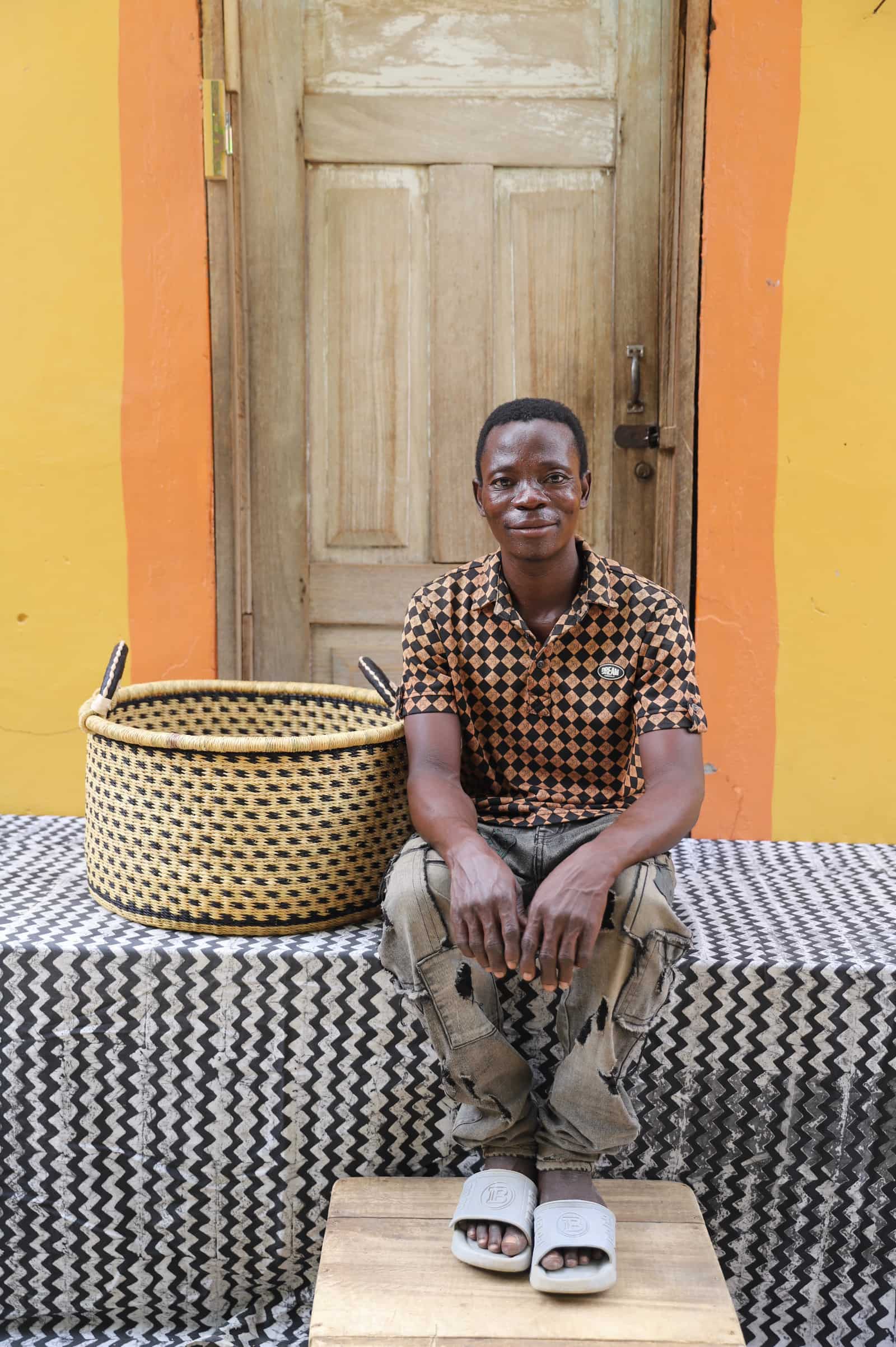 Woven Tub (Medium) with man weaver handwoven in Ghana sitting on black and white cloth and wooden door in background