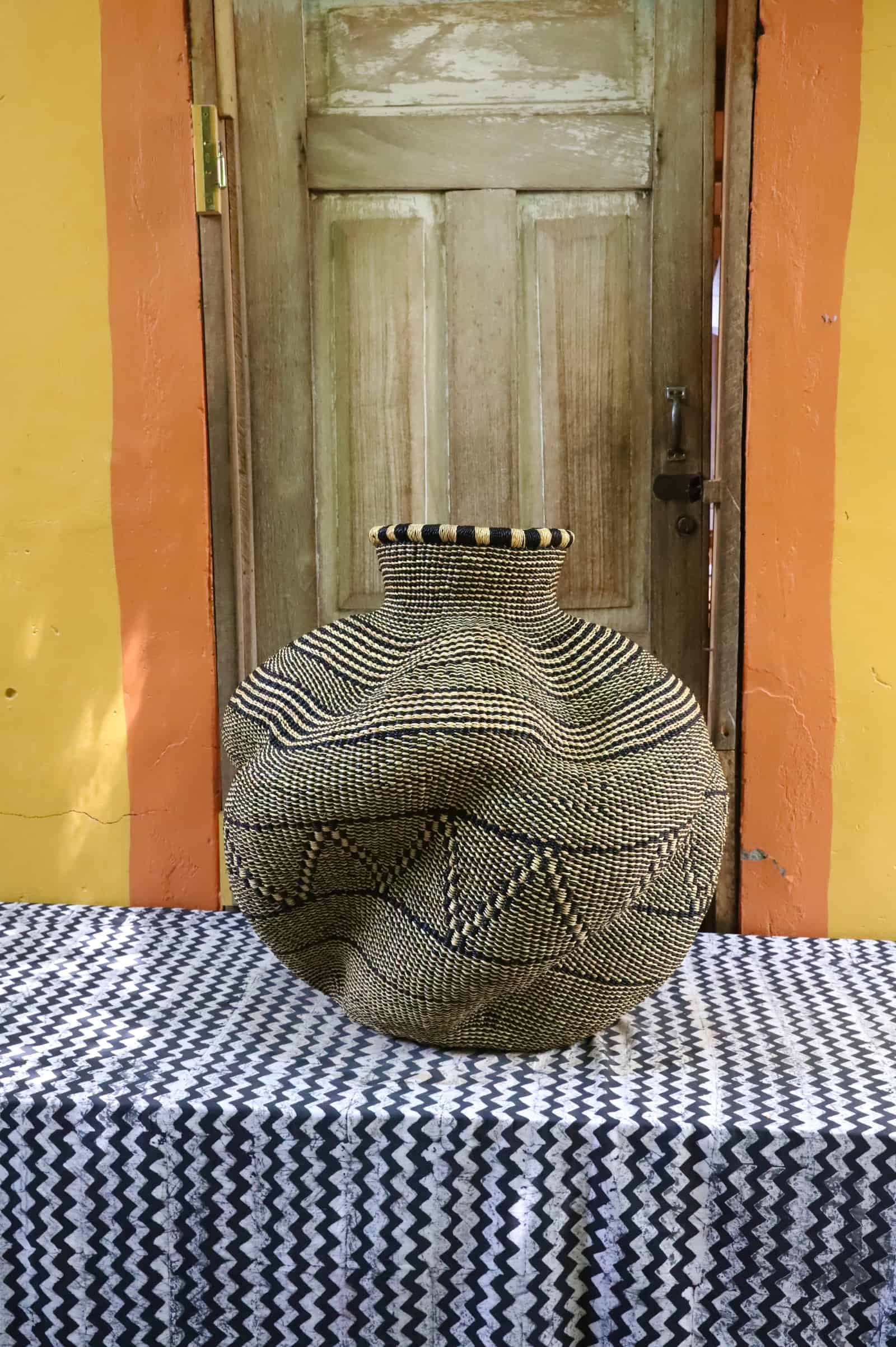 Front view of a large handwoven De-engo art basket with a round lobed form in natural straw and black geometric pattern.