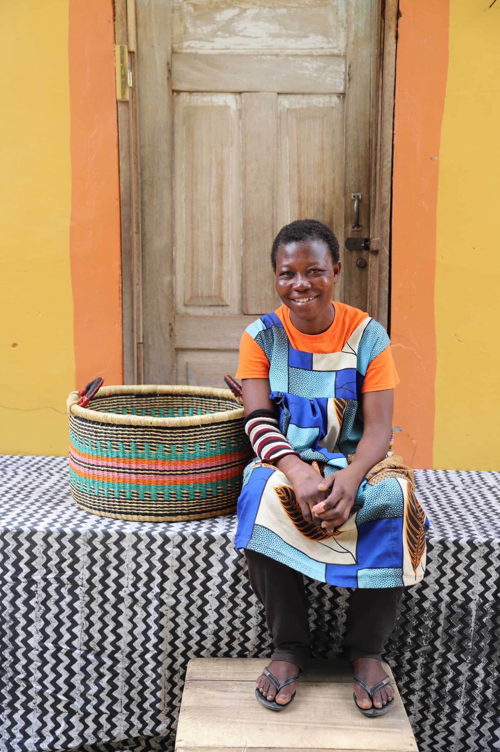Woven Tub (Medium) with woman weaver handwoven in Ghana sitting on black and white cloth and wooden door in background


