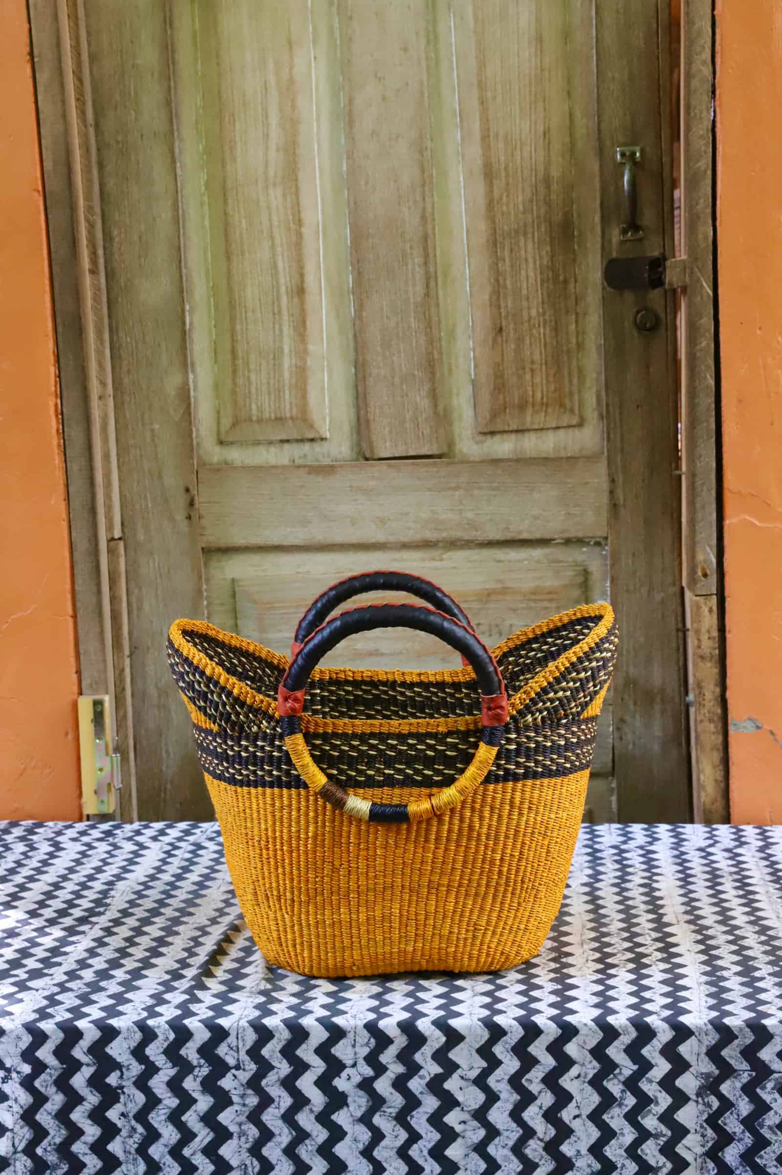Woven beach bag in vivid amber yellow with a black zigzag stripe and circular leather handles