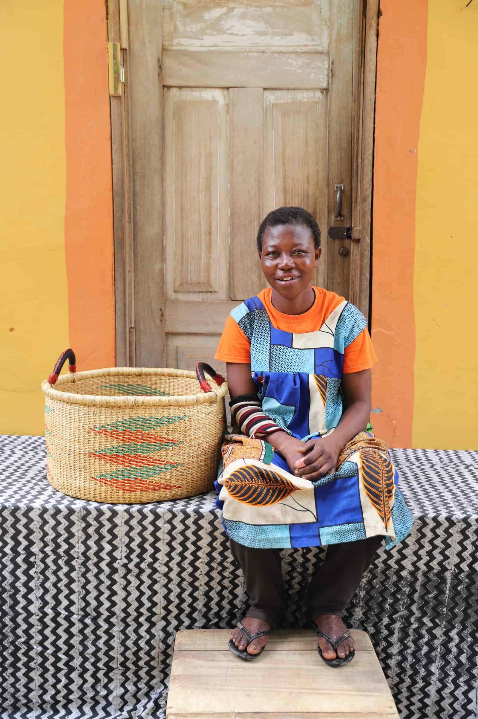 Woven Tub (Medium) with woman weaver handwoven in Ghana sitting on black and white cloth and wooden door in background