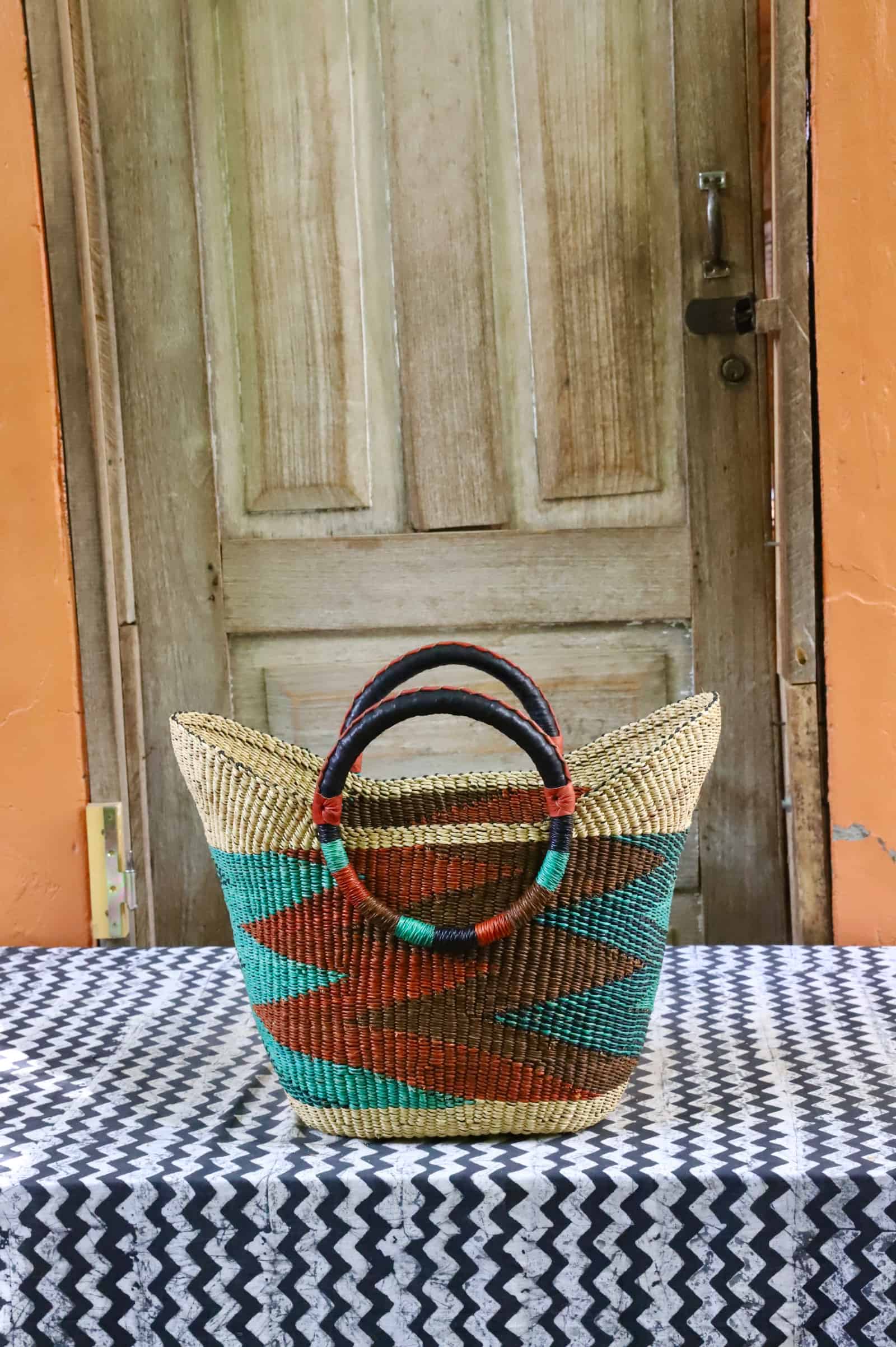 Woven beach bag in natural straw with teal and terracotta diagonal chevron pattern and dark handles