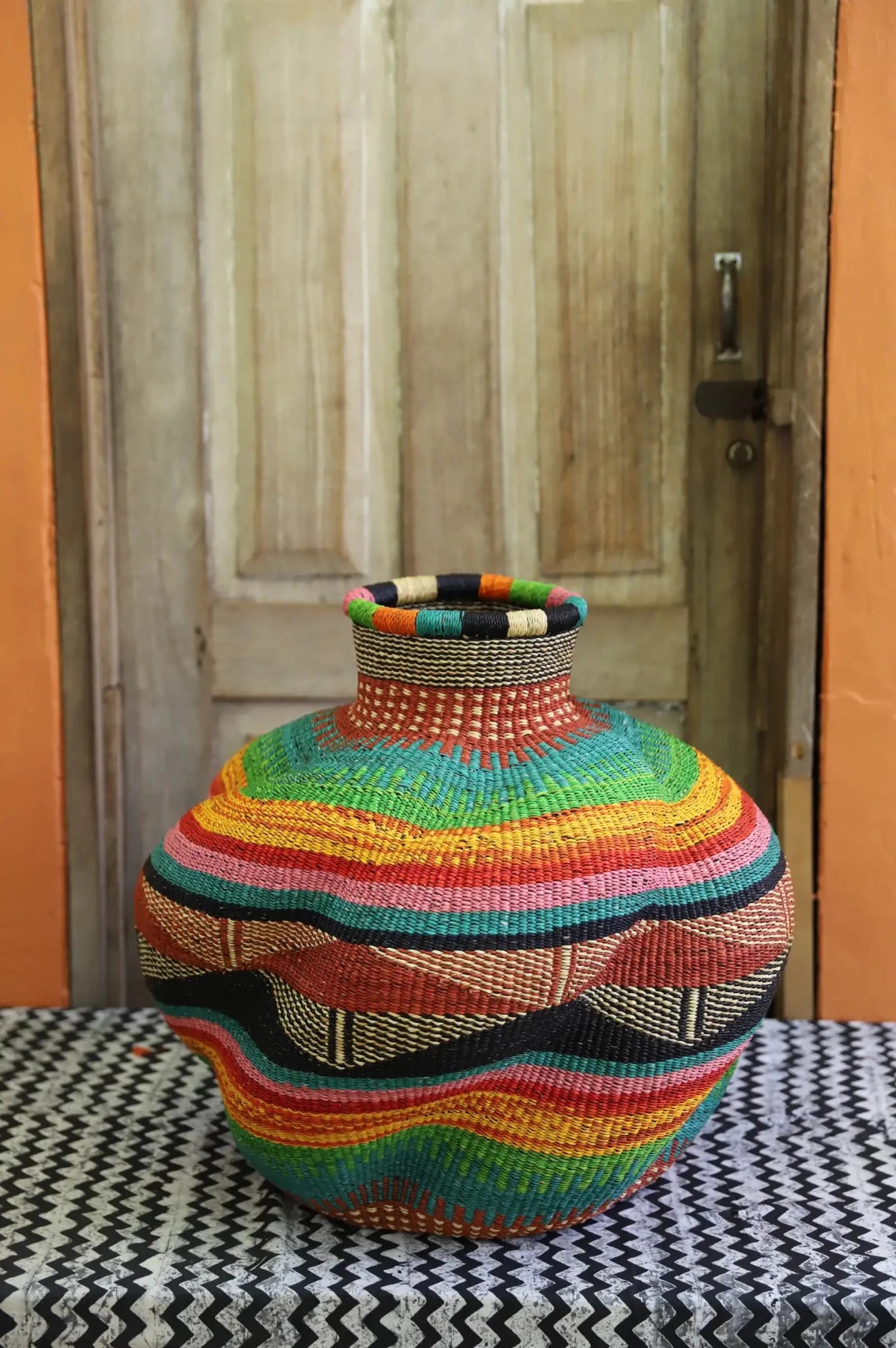 Multicolored woven piece on a patterned surface with a wooden door in the background