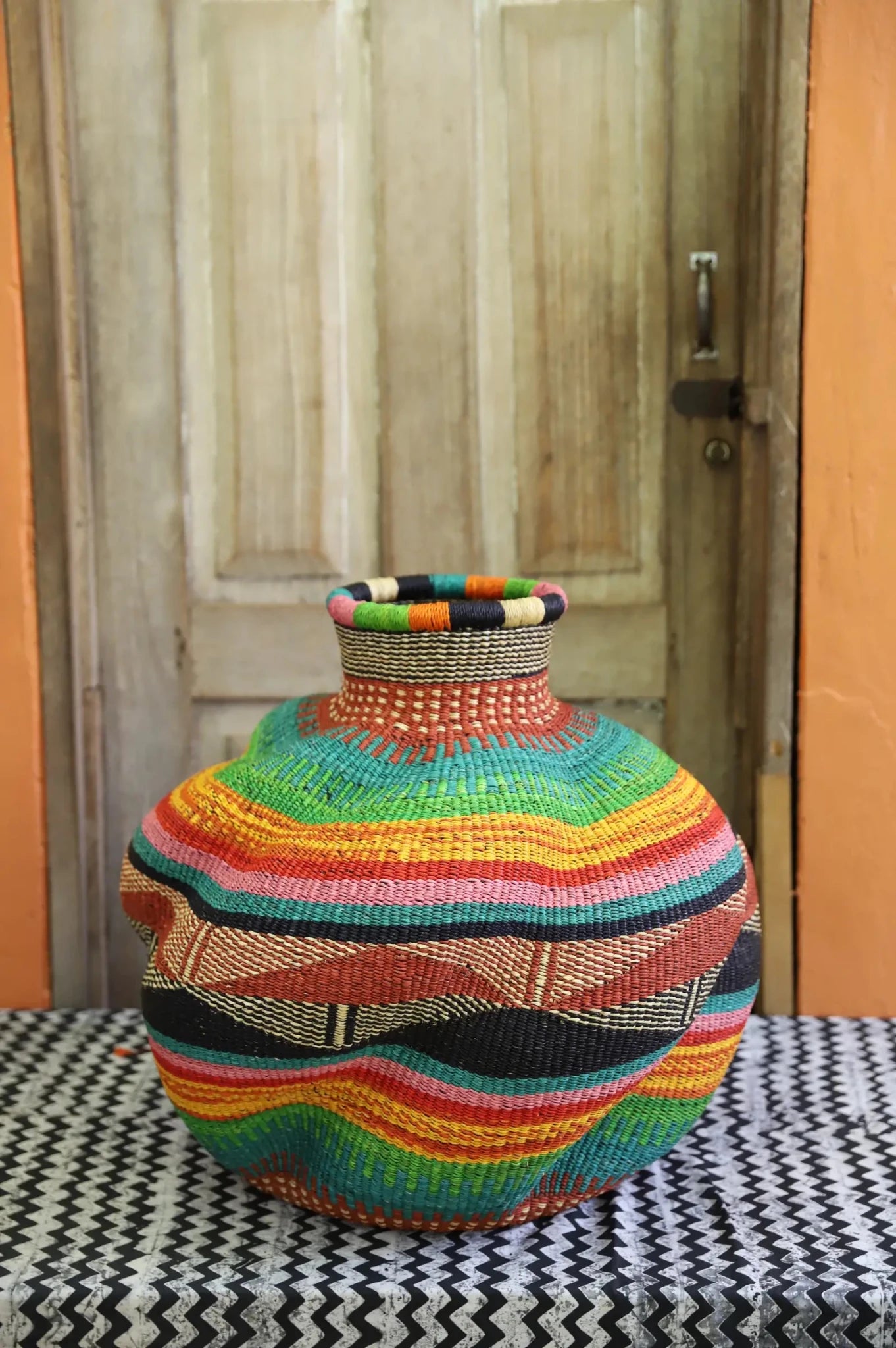 Colorful woven piece on a patterned surface with a wooden door in the background