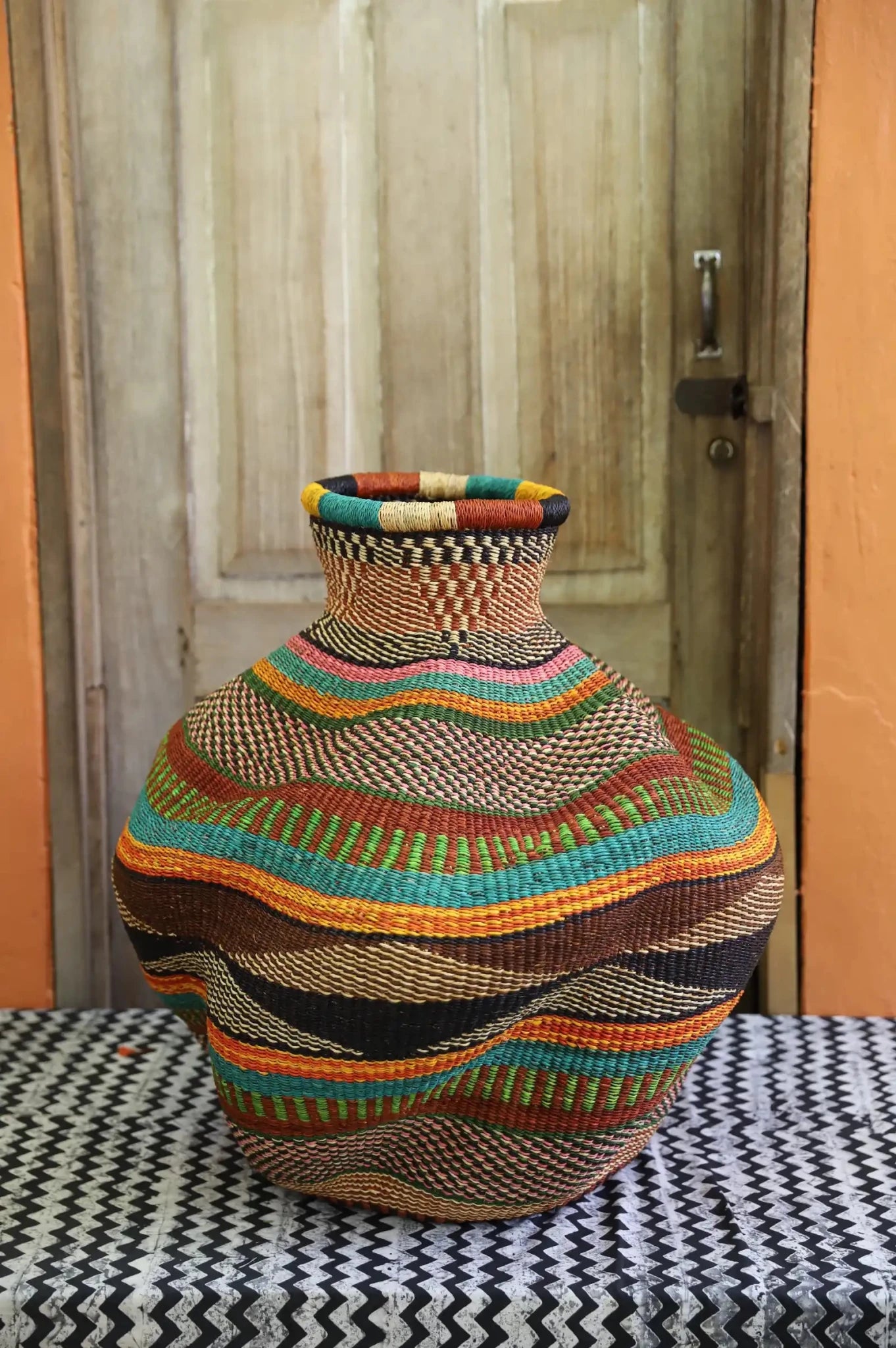 Colorful woven piece on a black and white patterned surface with a wooden door in the background.