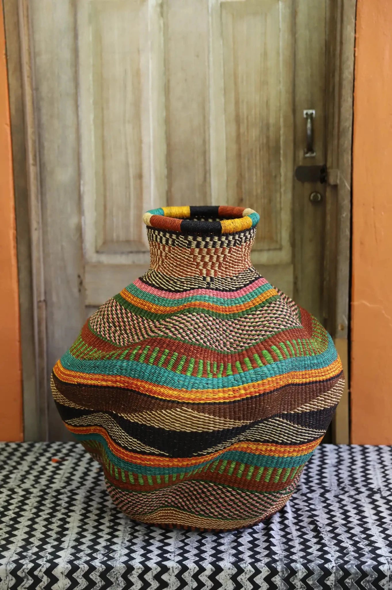 Colorful woven piece on a patterned surface with a wooden door in the background
