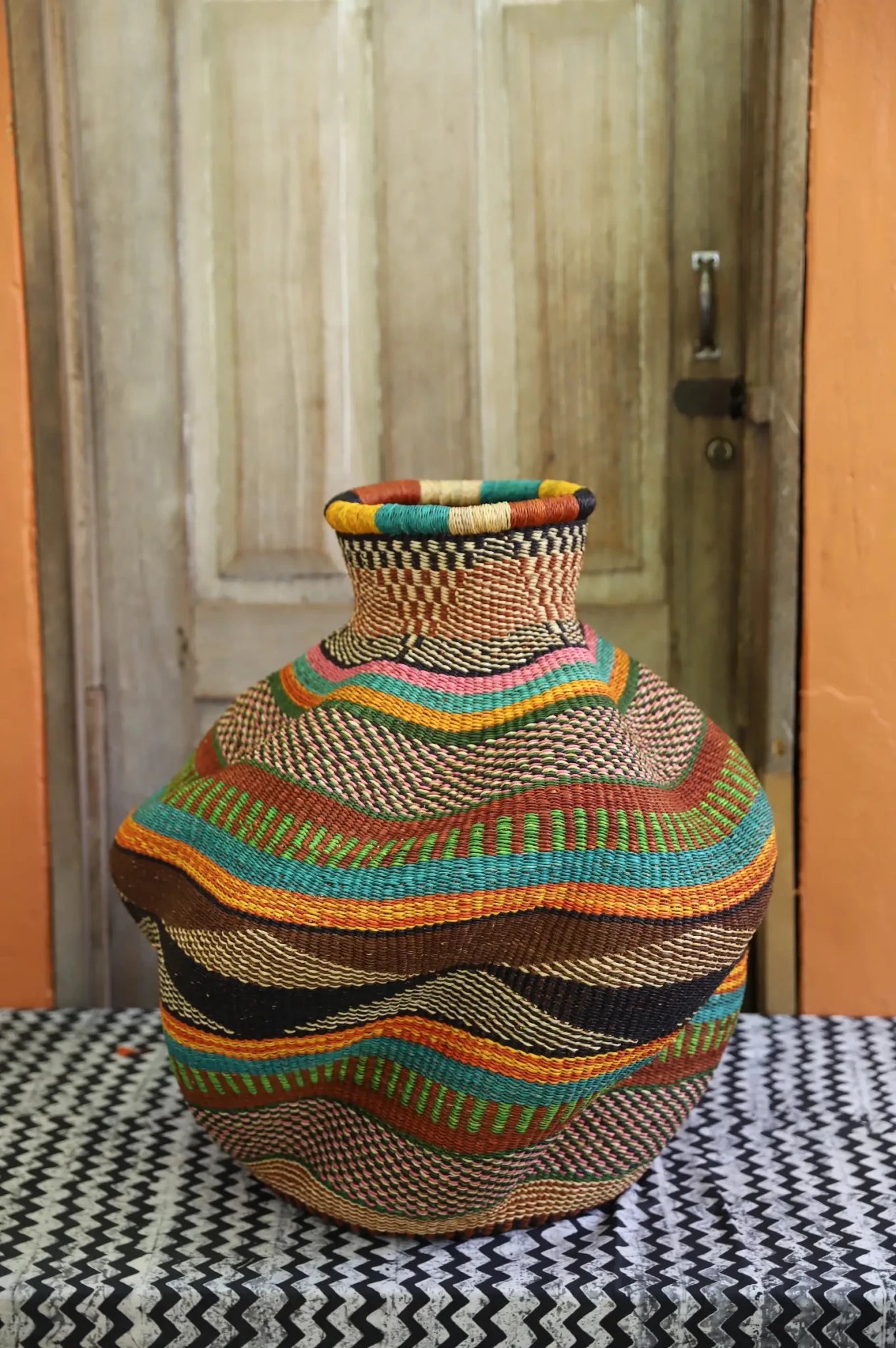 Multicolored woven piece on a patterned surface with a wooden door in the background