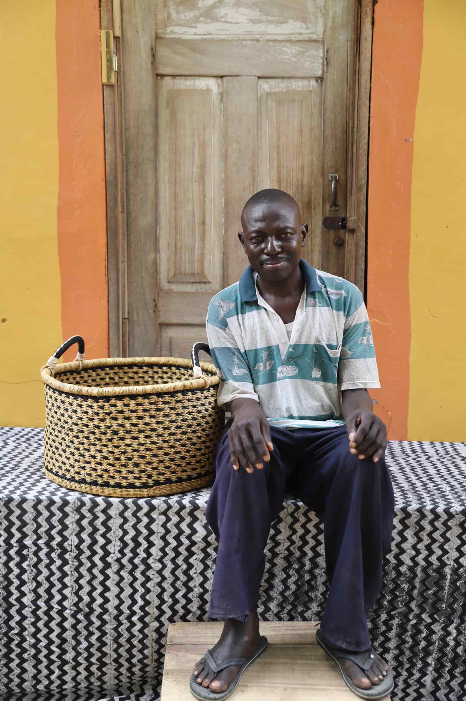 Woven Tub (Medium) with man weaver handwoven in Ghana sitting on black and white cloth and wooden door in background