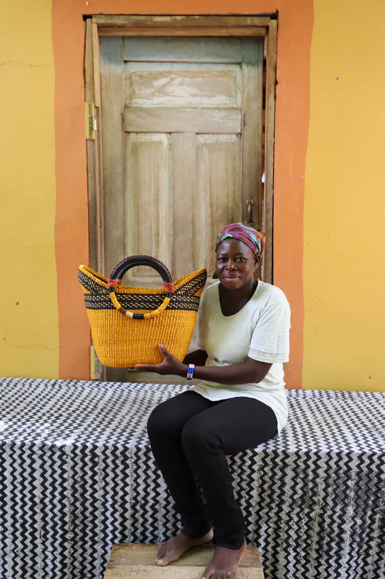 Woman in white top holding a woven beach bag in amber yellow with black stripe detail