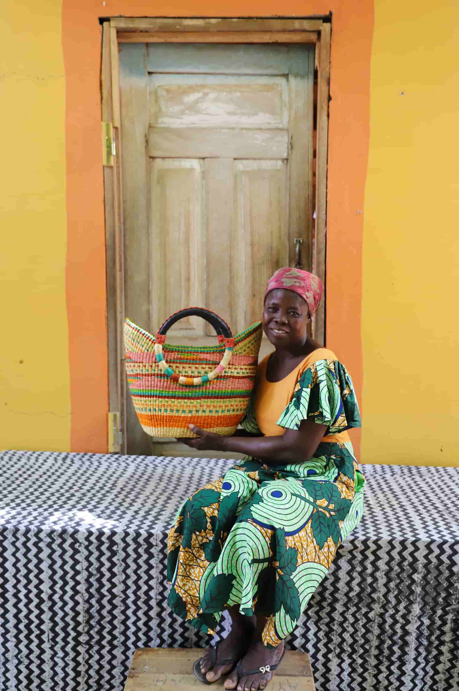 Woman in green and yellow print dress holding a woven beach bag in pink, green and terracotta stripes