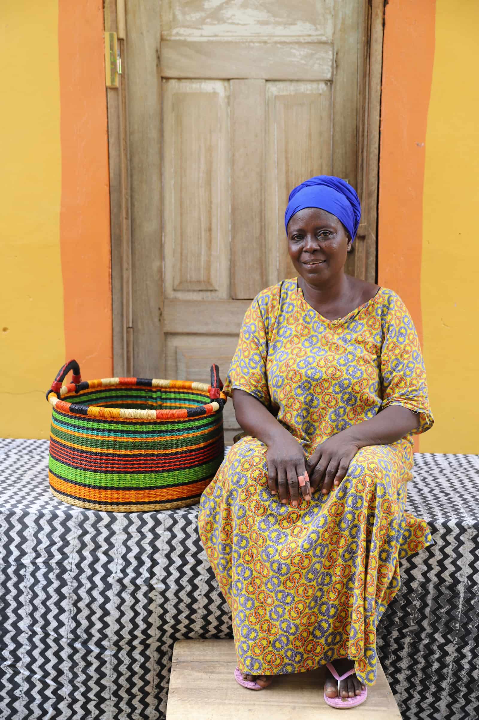 Woven Tub (Small) with woman weaver handwoven in Ghana sitting on black and white cloth and wooden door in background