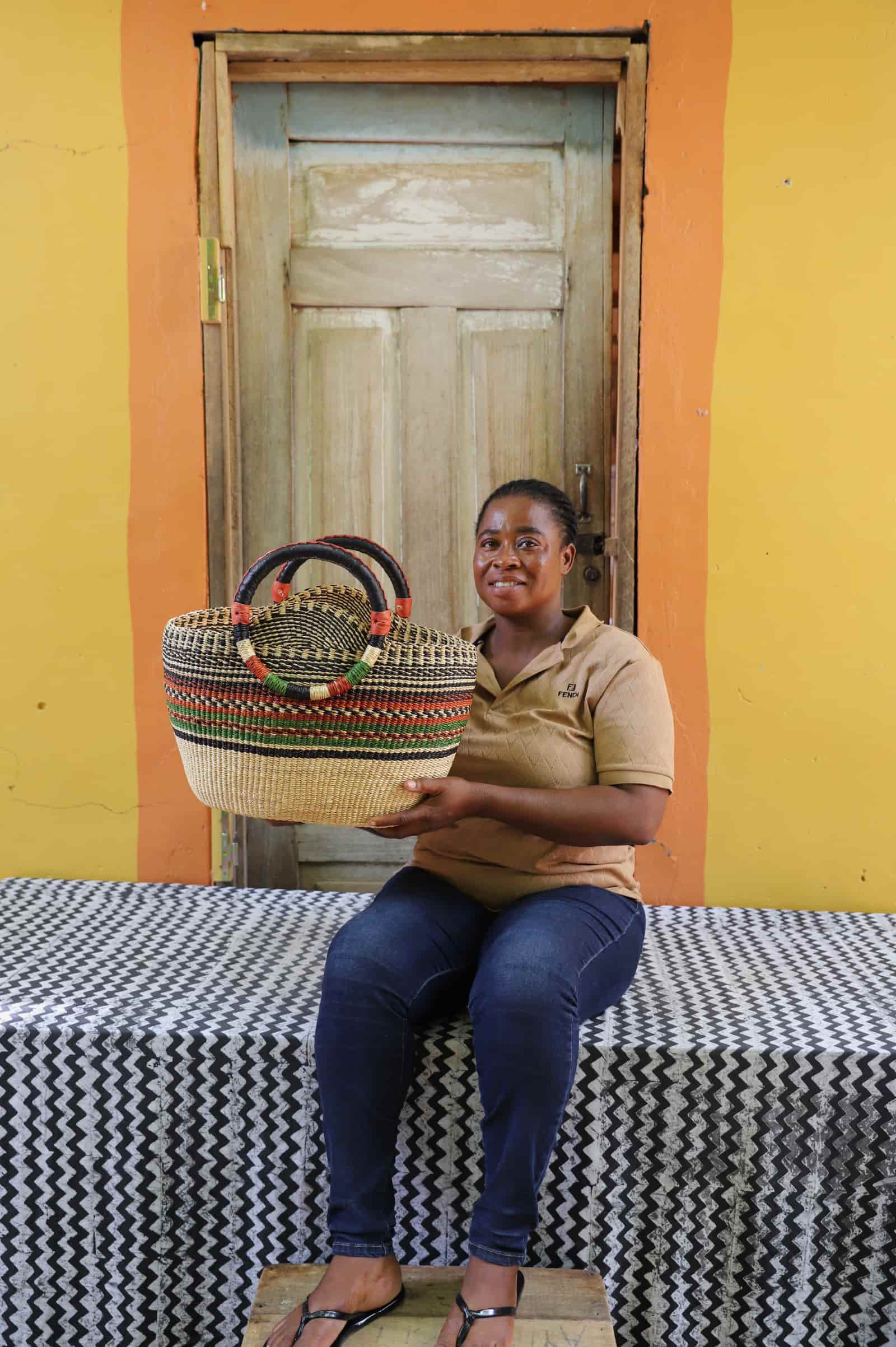 Woman holding a colorful woven carry on bag on a black and white cloth against a wooden door.