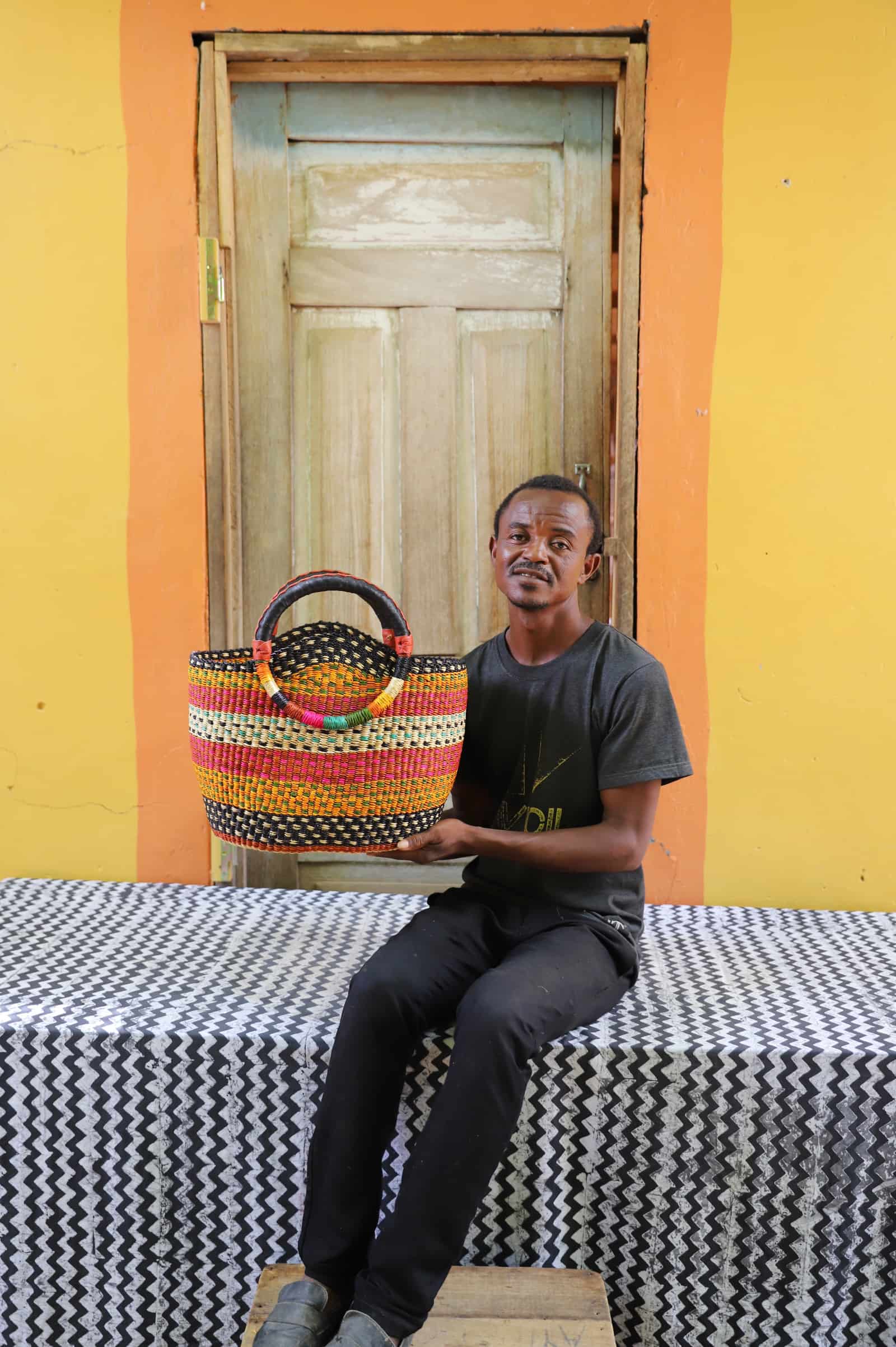Man holding a colorful woven carry on bag on a black and white cloth against a wooden door.
