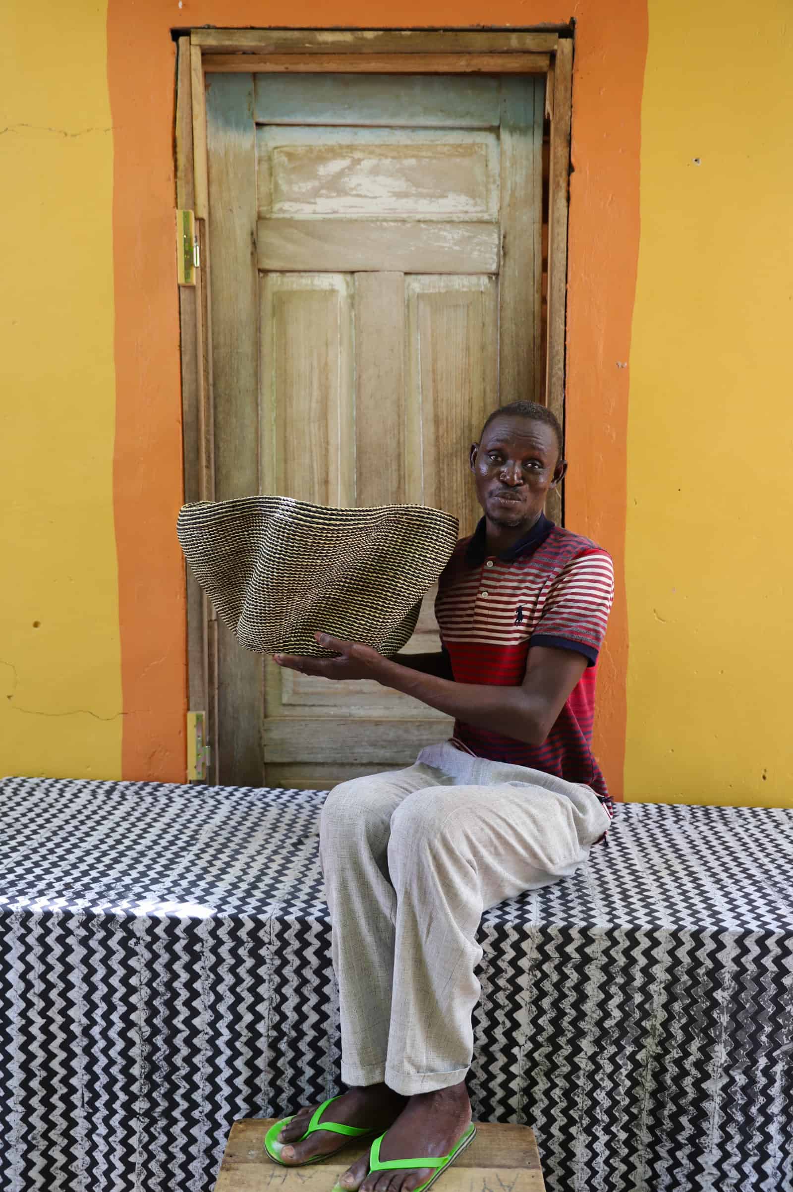 Artisan holding a decorative woven basket  on a black and white cloth against a wooden door.