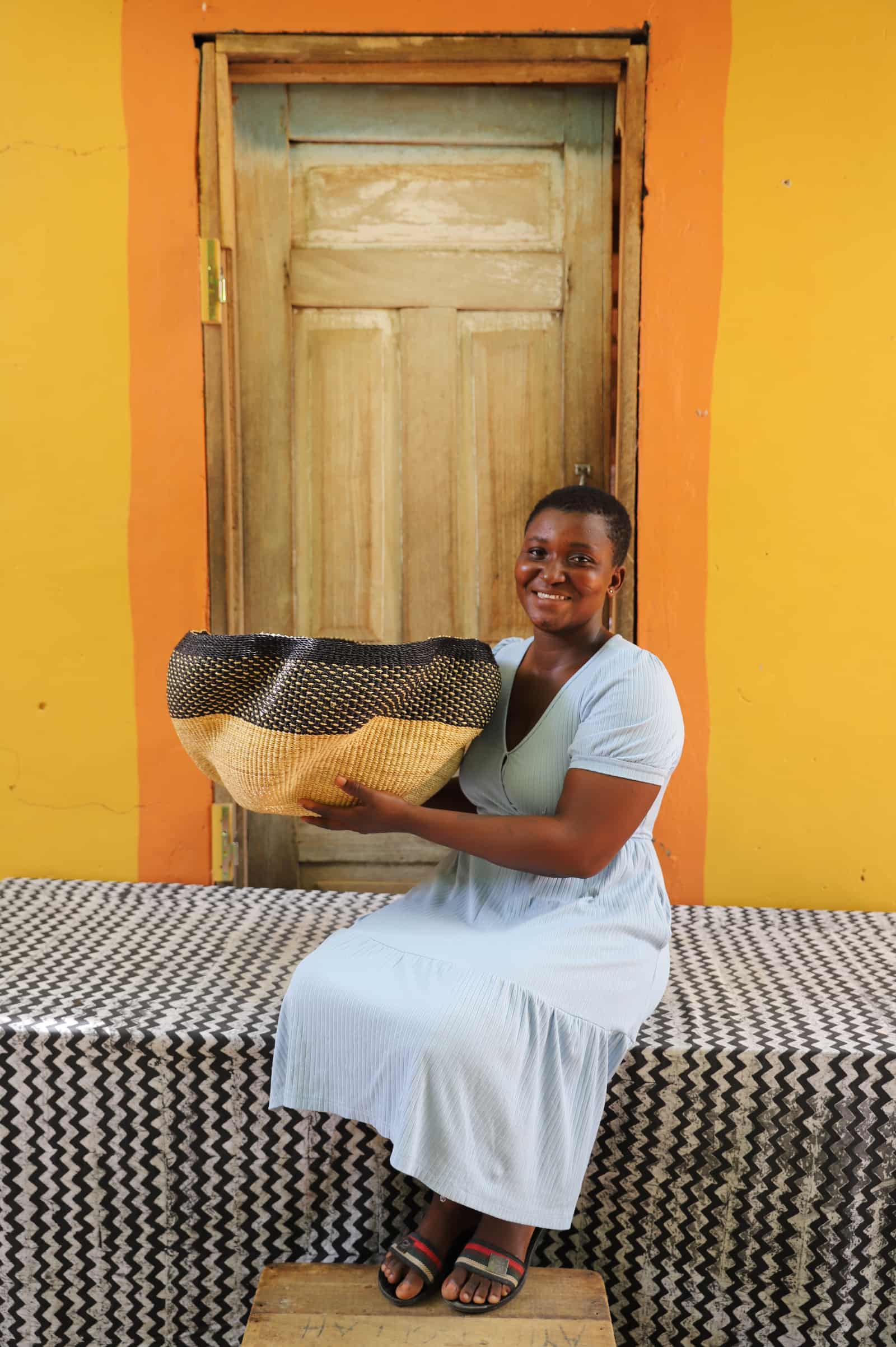 Artisan holding a decorative woven basket  on a black and white cloth against a wooden door.