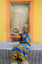 Woman holding a woven basket in front of a yellow wall with a wooden door.