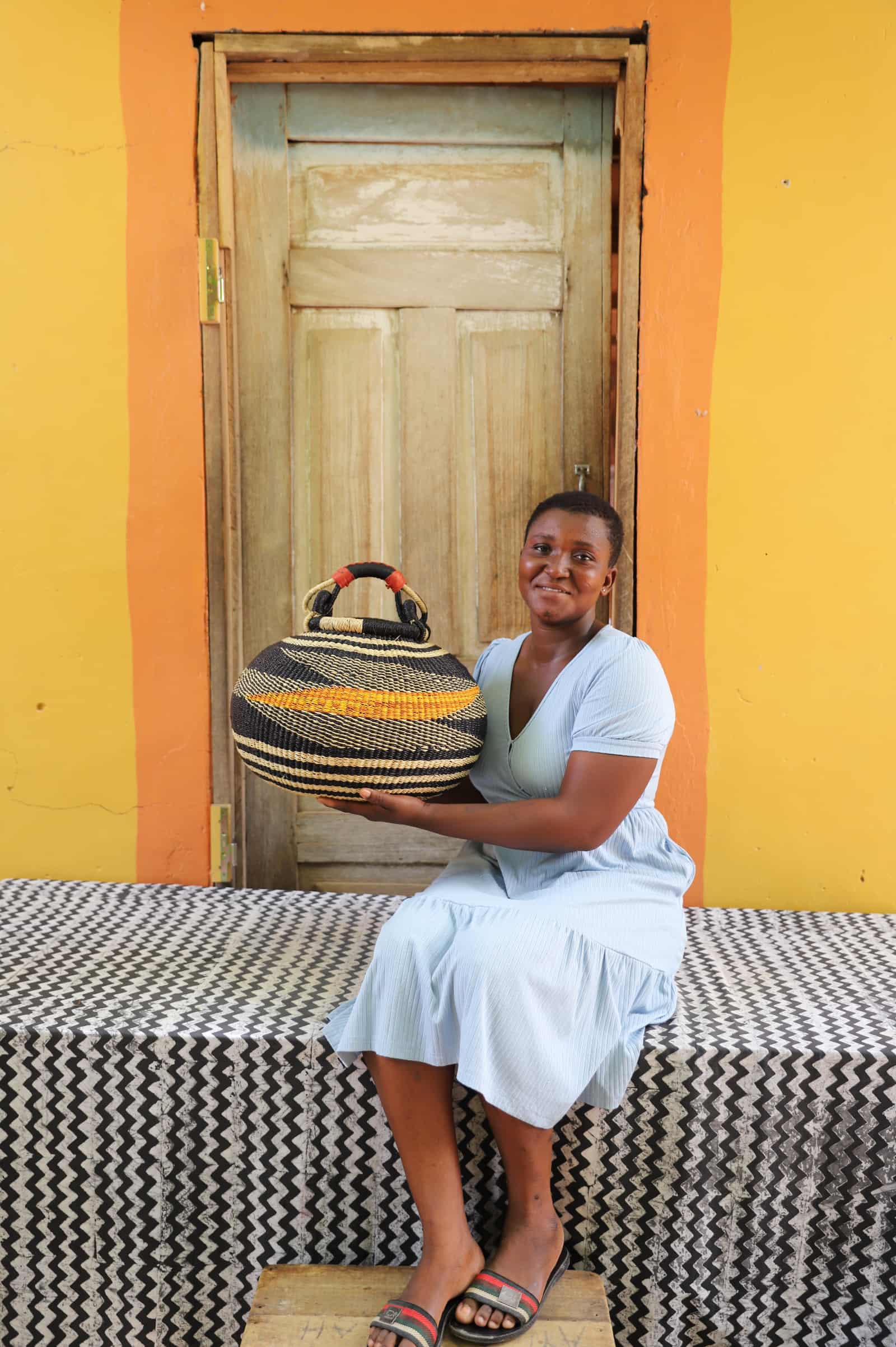 Large pot storage basket in black and natural straw with amber stripe, carried by woman