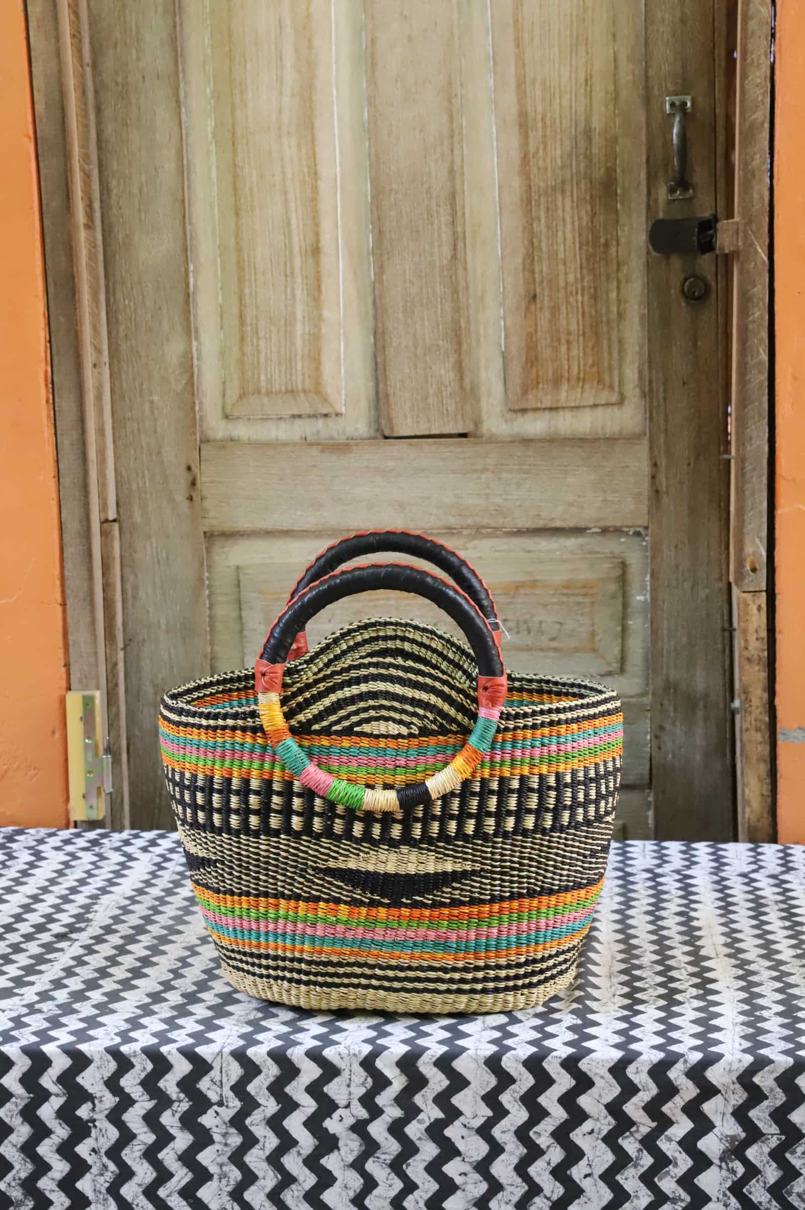 Colorful woven carry on bag on a black and white cloth against a wooden door.
