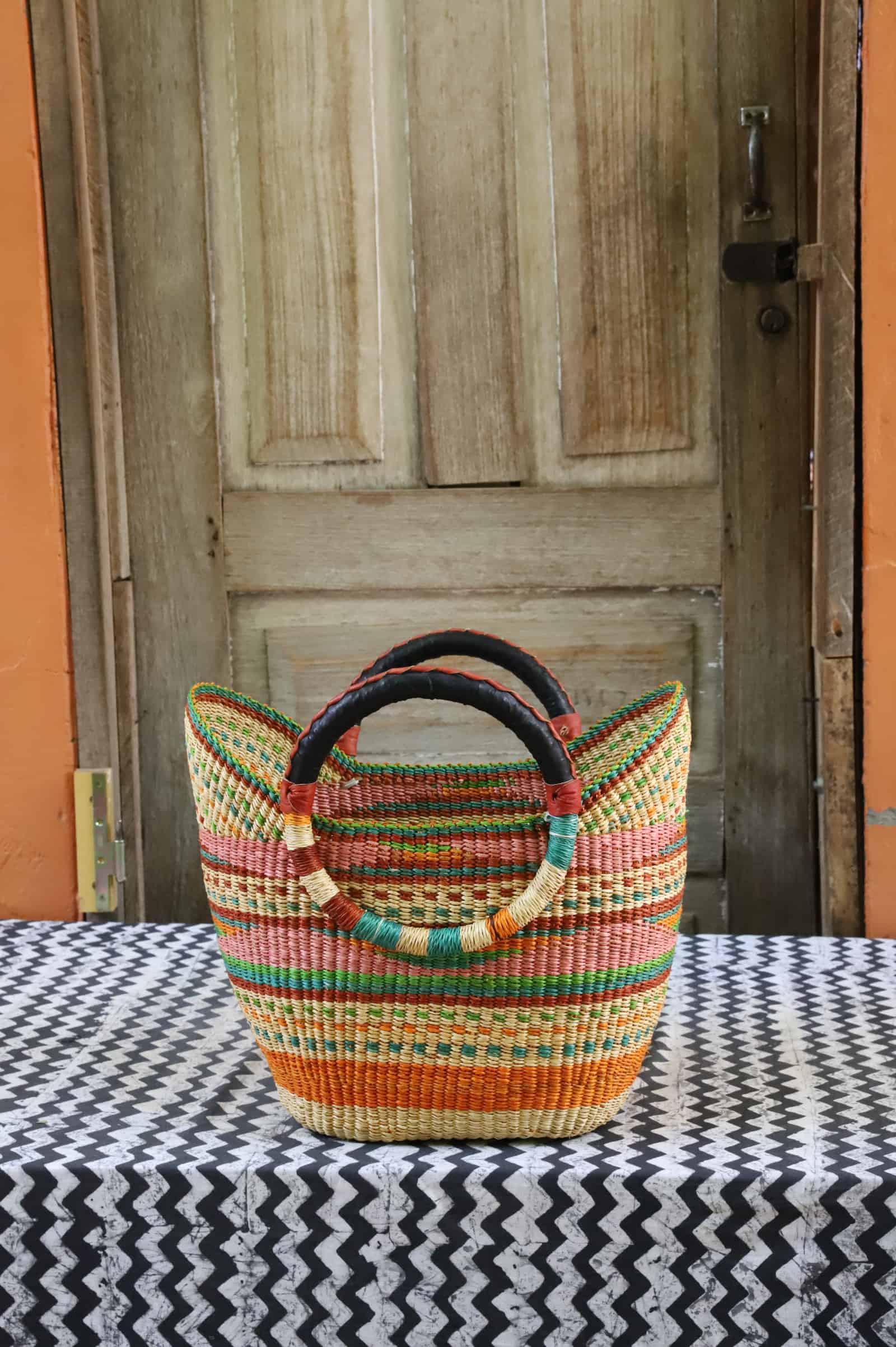 Woven beach bag in earth-tone stripes of pink, green and terracotta with circular leather handles