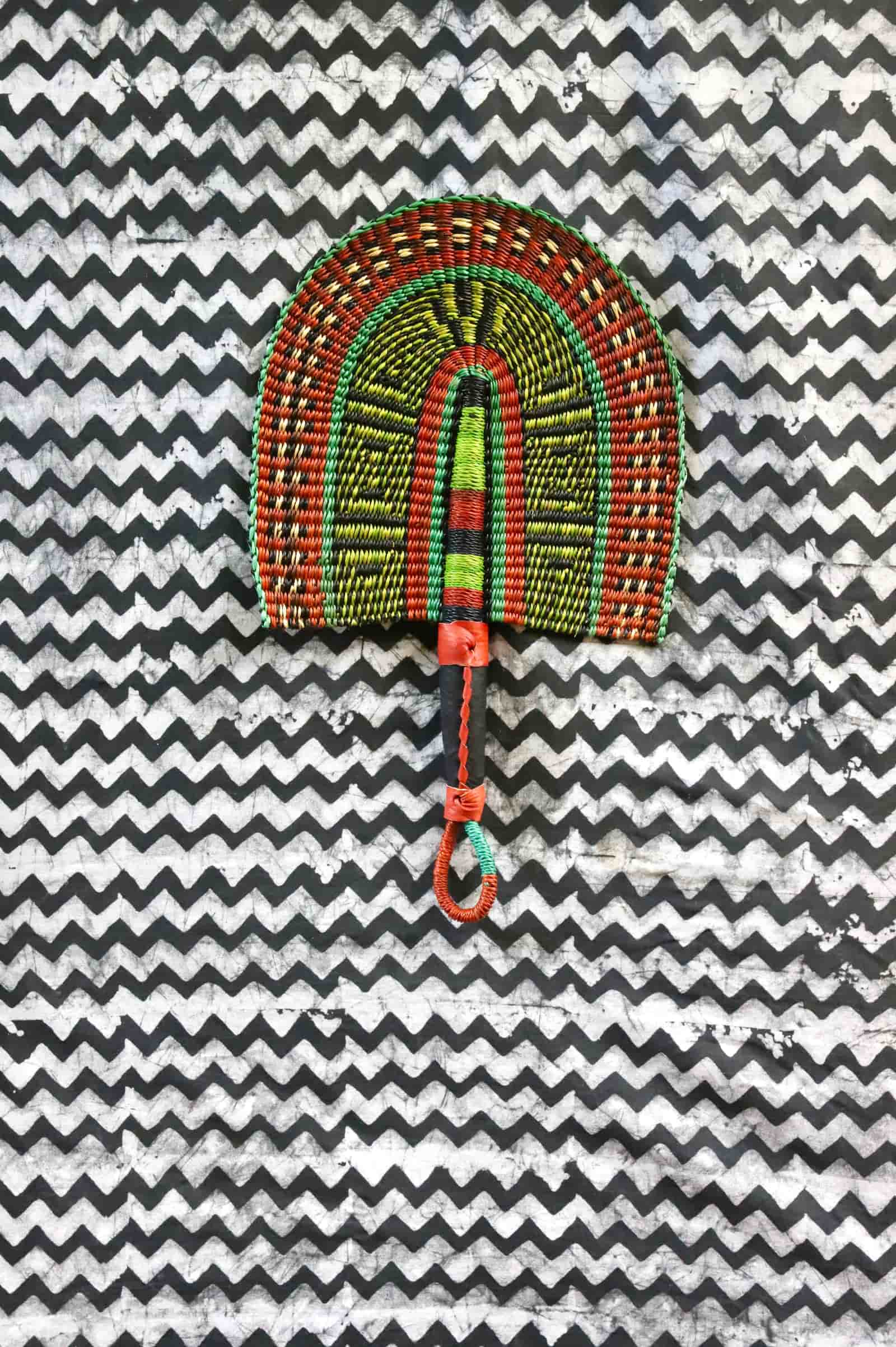 Handwoven Bolga fan with an orange and lime geometric arch pattern, on a black and white chevron cloth.