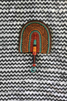 Handwoven Bolga fan with a dark brown body and teal concentric arch outlines, teal loop handle, on a chevron cloth.