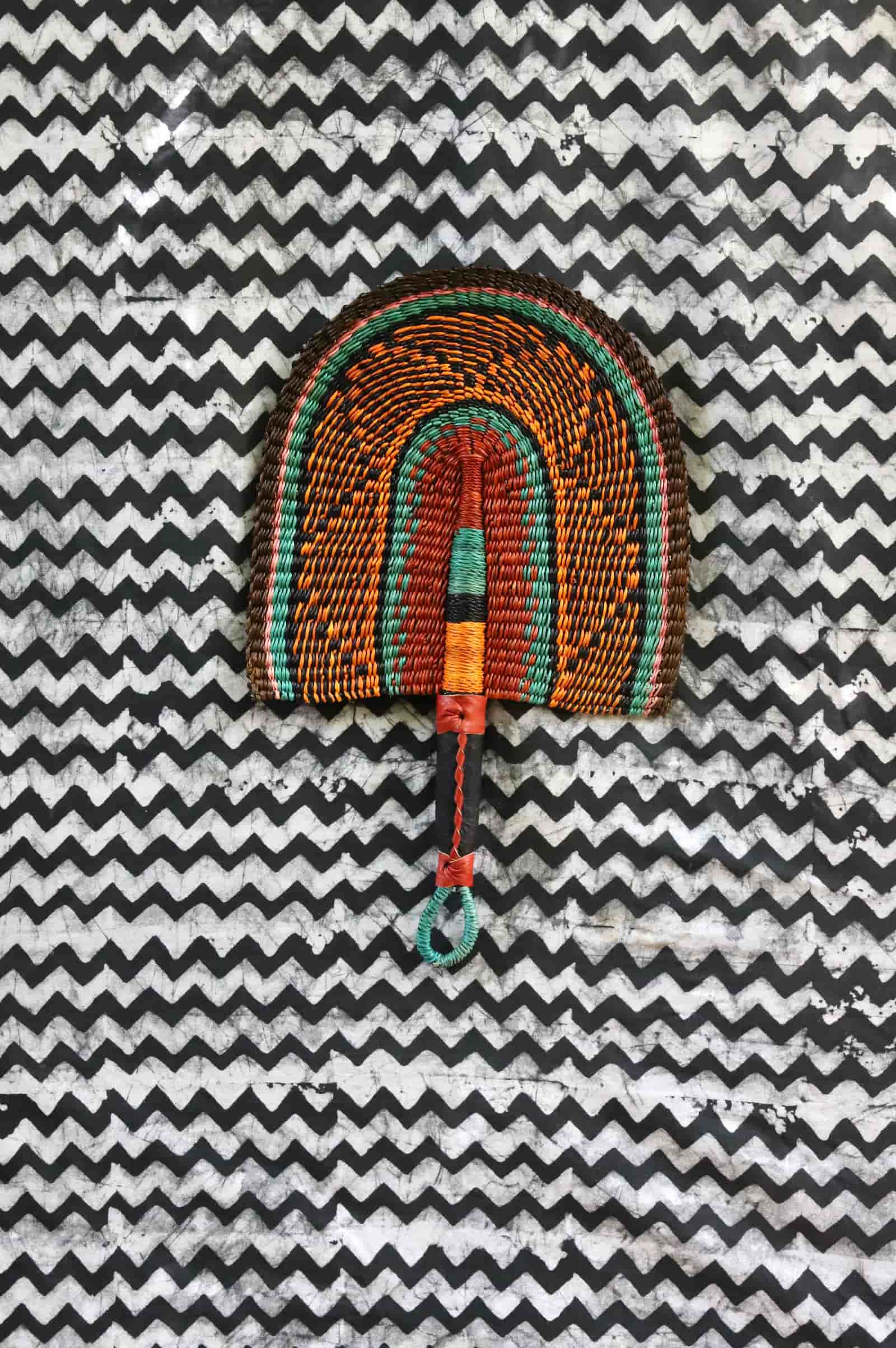 Handwoven Bolga fan with a dark brown body and teal concentric arch outlines, teal loop handle, on a chevron cloth.