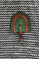 Handwoven Bolga fan in green and terracotta concentric arch, speckled detailing, on a black and white chevron cloth.