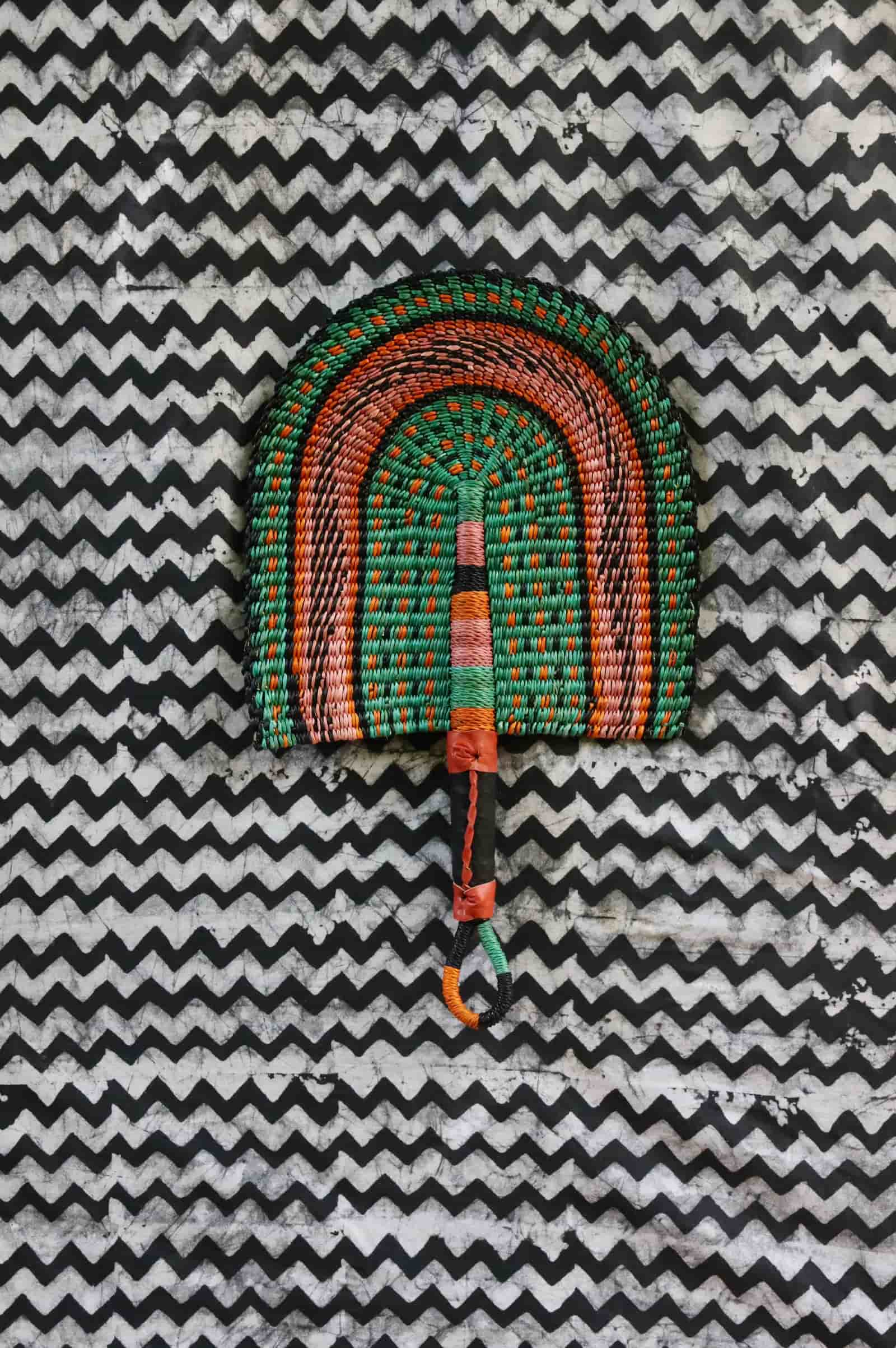 Handwoven Bolga fan in green and terracotta concentric arch, speckled detailing, on a black and white chevron cloth.