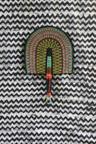 Handwoven Bolga fan with a green and pink concentric arch pattern, on a black and white chevron cloth.