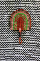 Handwoven Bolga fan in terracotta, green and pink concentric arch pattern, tan leather handle, on a chevron cloth.