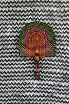 Handwoven Bolga fan with green, pink and amber concentric arch pattern, on a black and white chevron cloth.