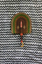 Handwoven Bolga fan in dark brown with green and amber speckled arches, on a black and white chevron cloth.