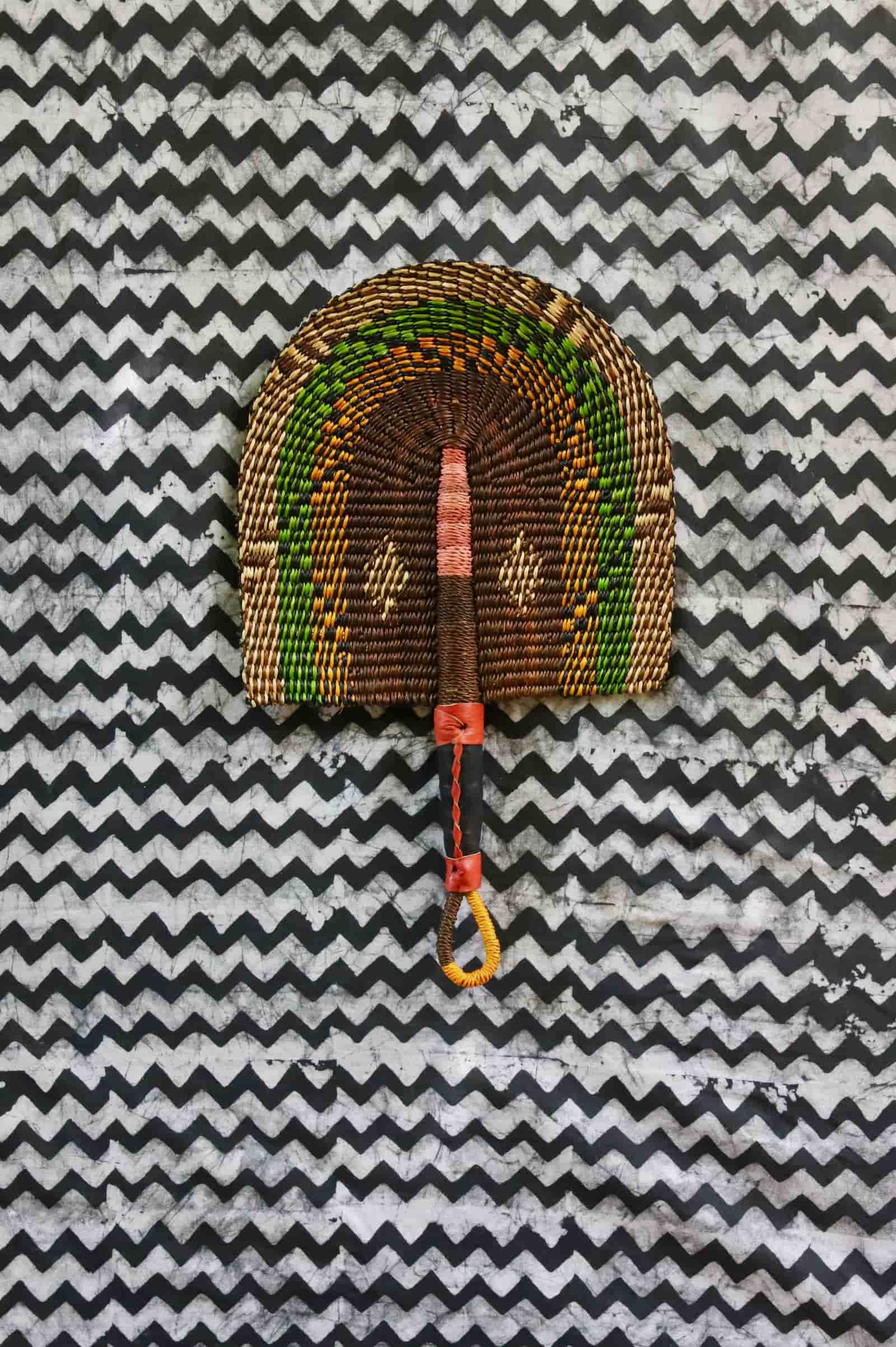 Handwoven Bolga fan in dark brown with green and amber speckled arches, on a black and white chevron cloth.