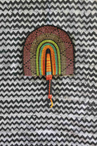 Handwoven Bolga fan with a multicolour concentric arch pattern in pink, green and amber, on a black and white chevron cloth.