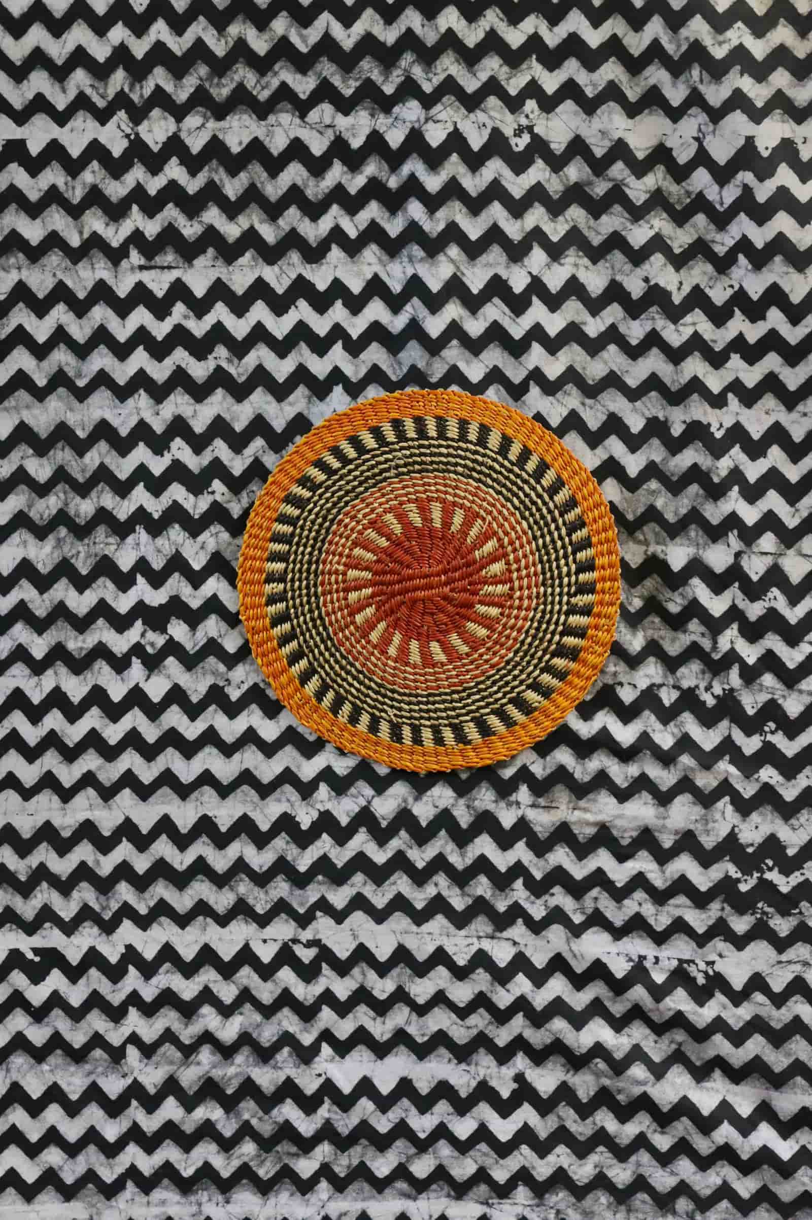 Small woven placemat with terracotta and olive radial pattern, natural straw outer ring