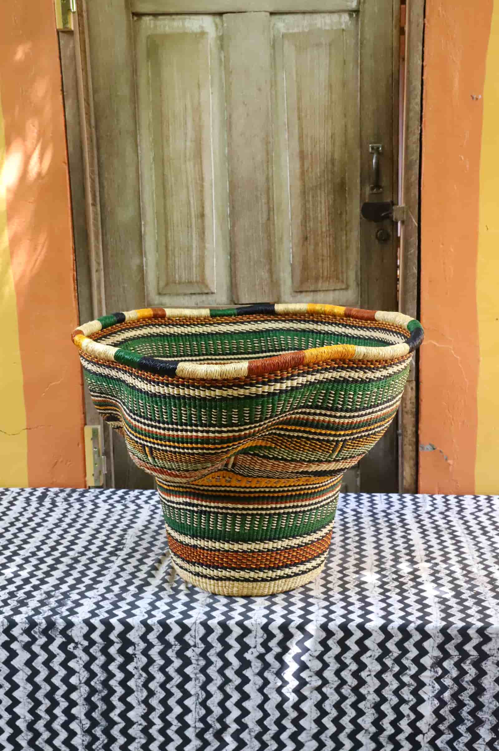 Wave planter in green and terracotta wave pattern, wide open-topped woven form on chevron cloth against a wooden door.