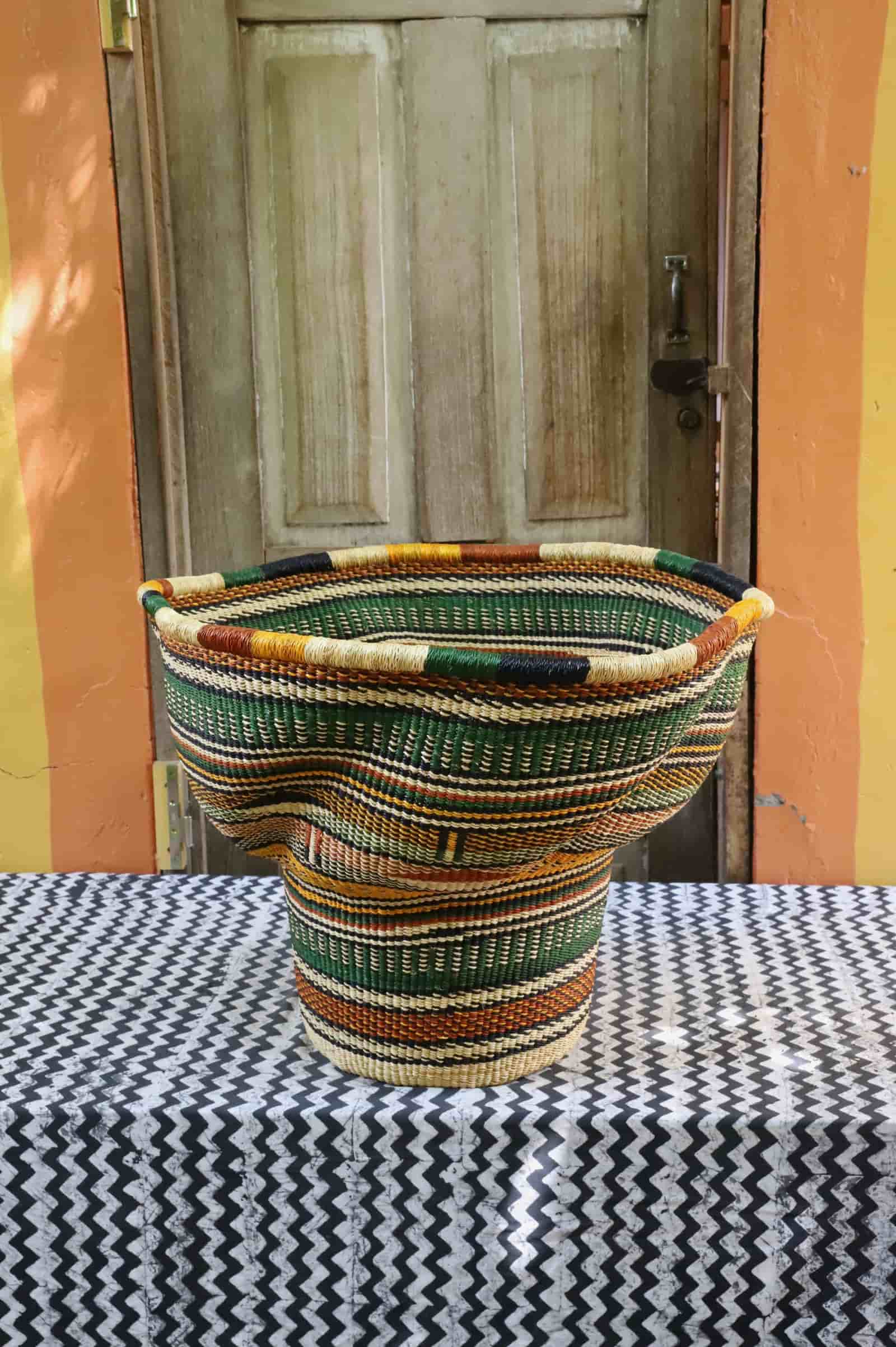 Wave planter in green, terracotta and natural stripes, wide open-topped woven form on chevron cloth against a wooden door.