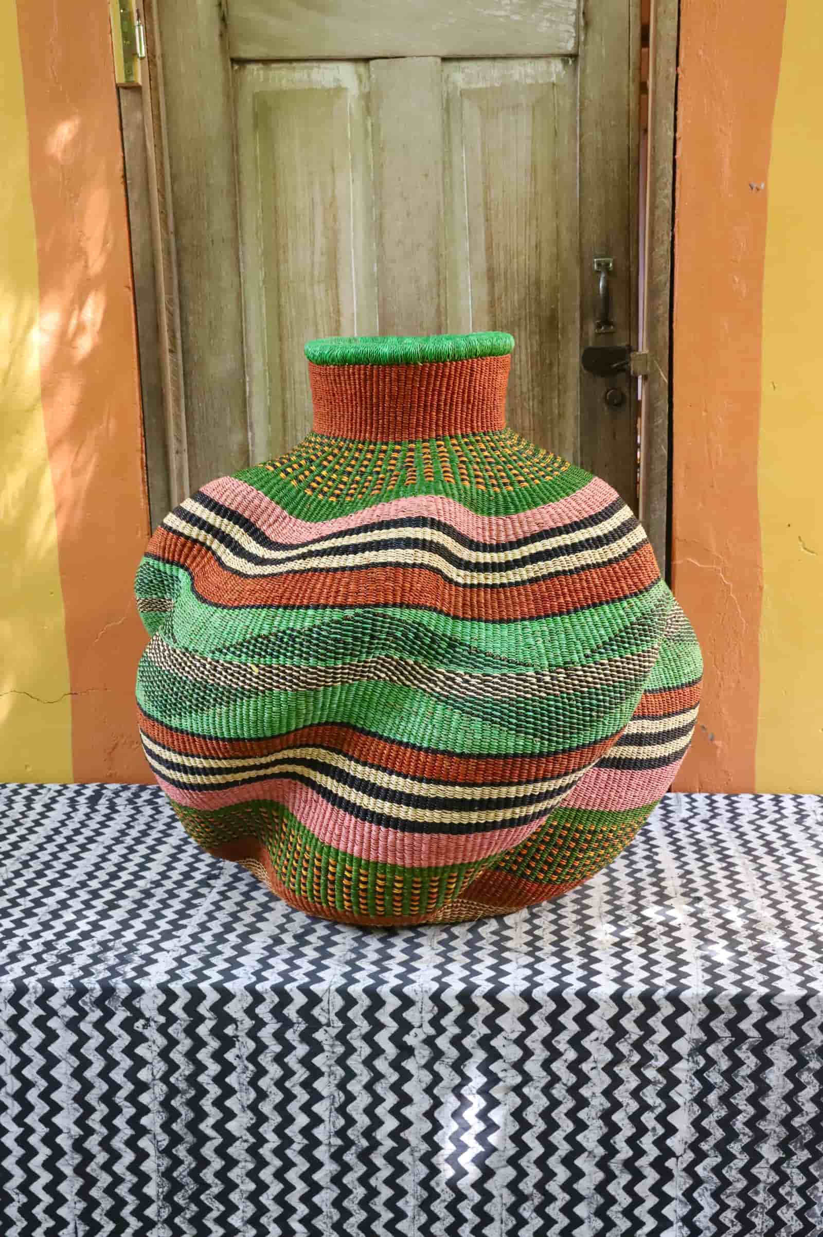 Large handwoven De-engo art basket with a lobed form in green, terracotta and pink stripes, on a chevron cloth.