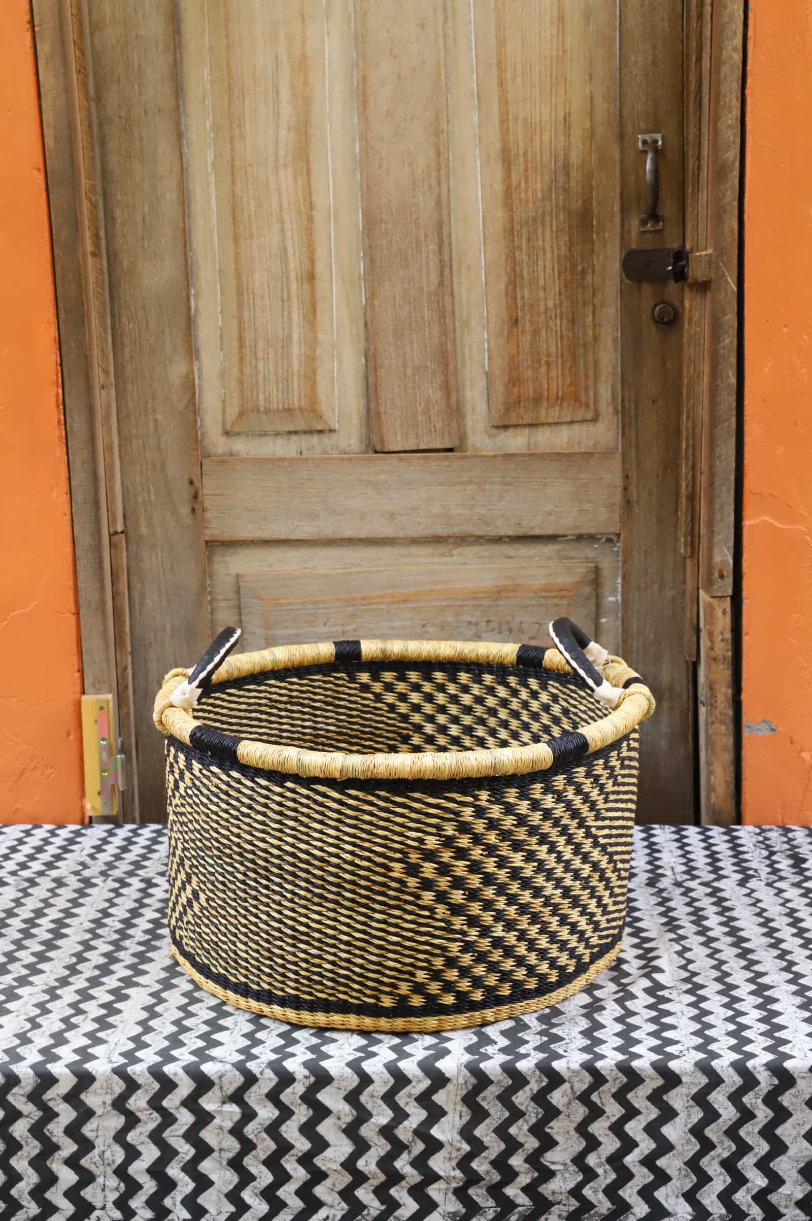 Woven Tub (Medium) handwoven in Ghana sitting on black and white cloth with wooden door background

